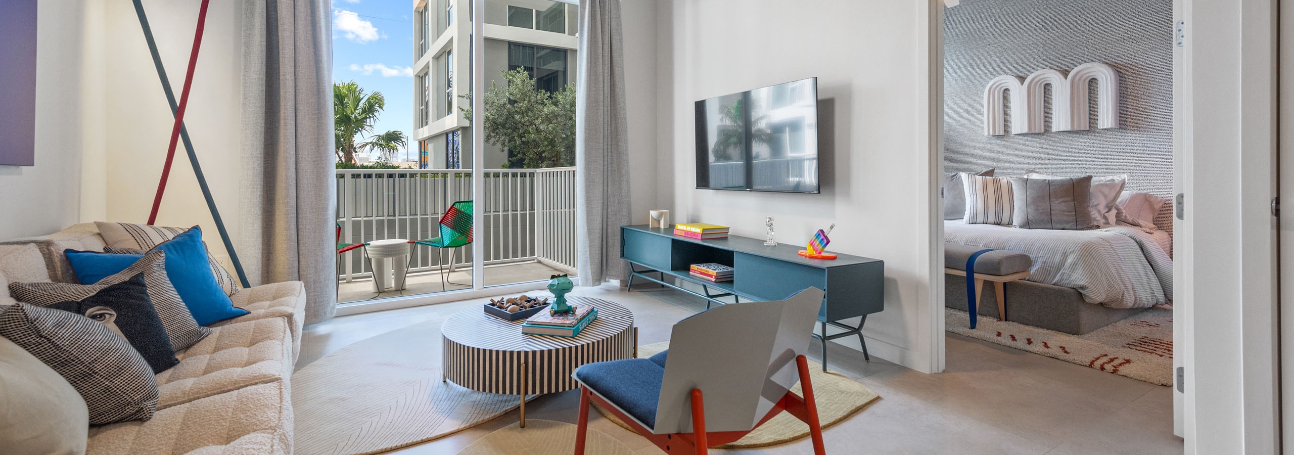 Living room at AMLI Wynwood apartments with whimsical designer furniture and views of a balcony with seating and bedroom with artwork