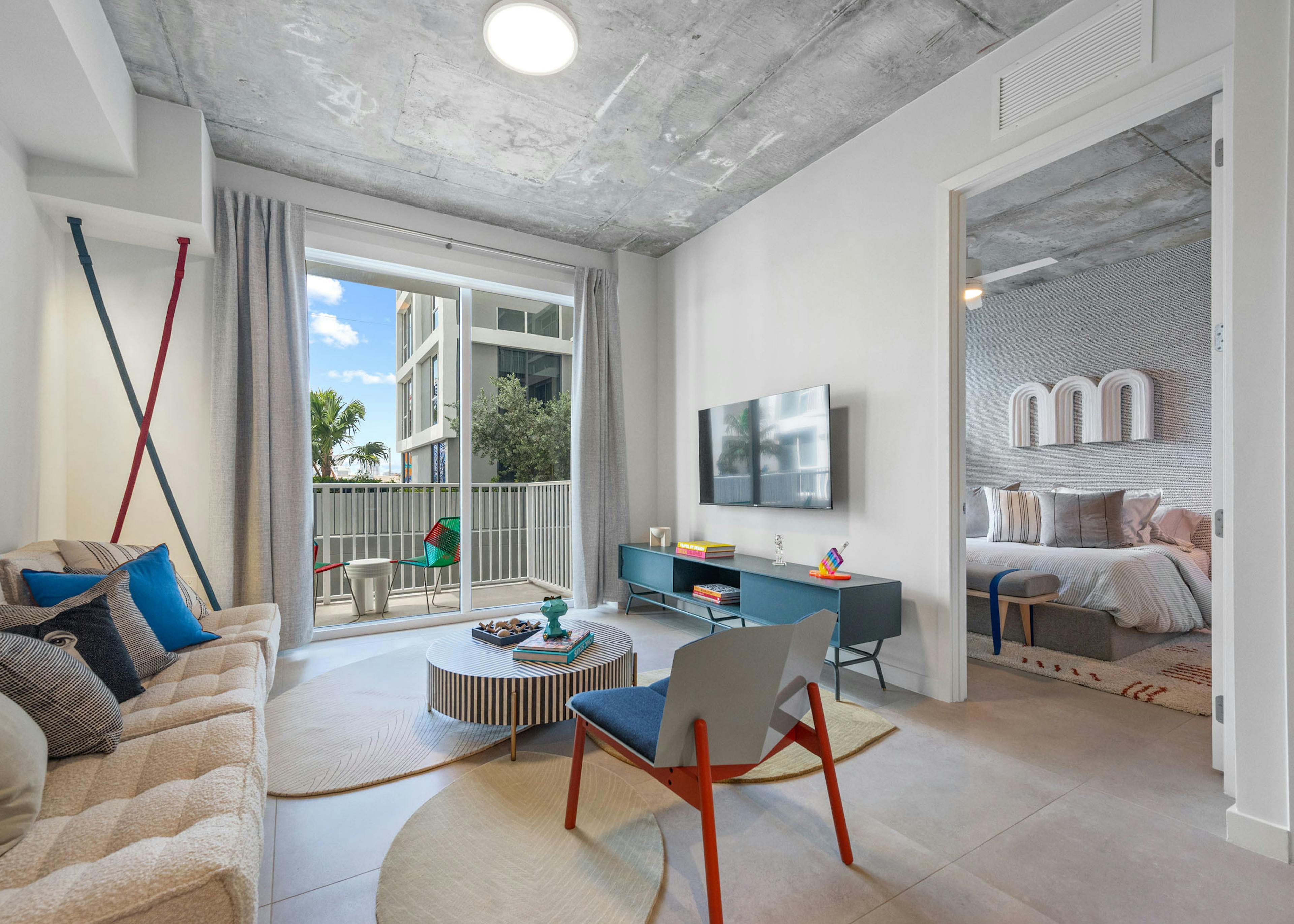 Living room at AMLI Wynwood apartments with whimsical designer furniture and views of a patio with seating and bedroom with artwork