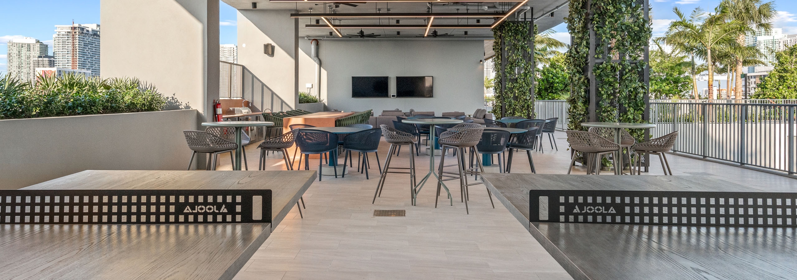 A covered rooftop sky lounge at AMLI Wynwood apartments with two table tennis tables and bistro seating tables and chairs
