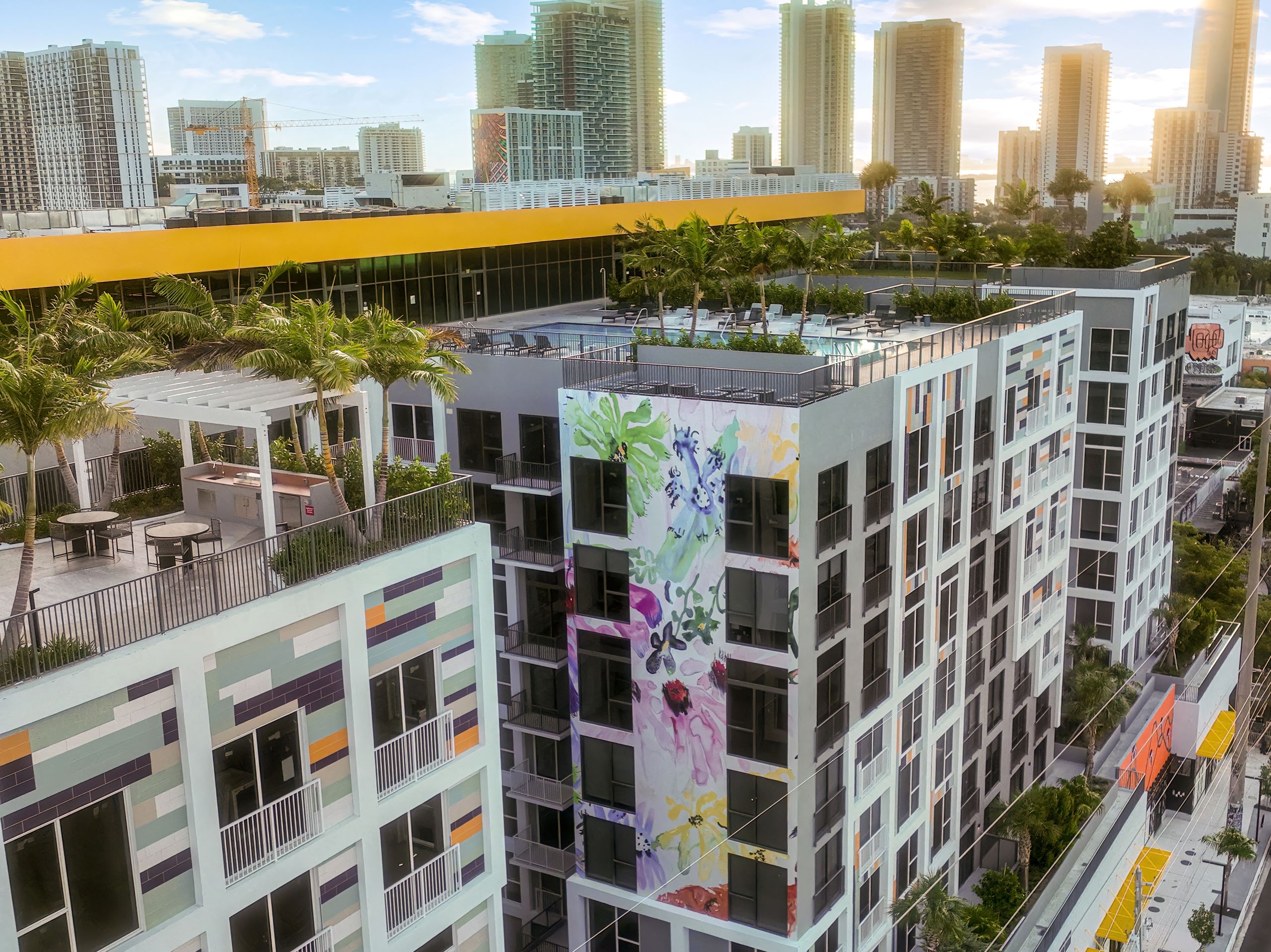 An aerial view of AMLI Wynwood apartment building adorned with a colorful floral mural with skyline in the distance