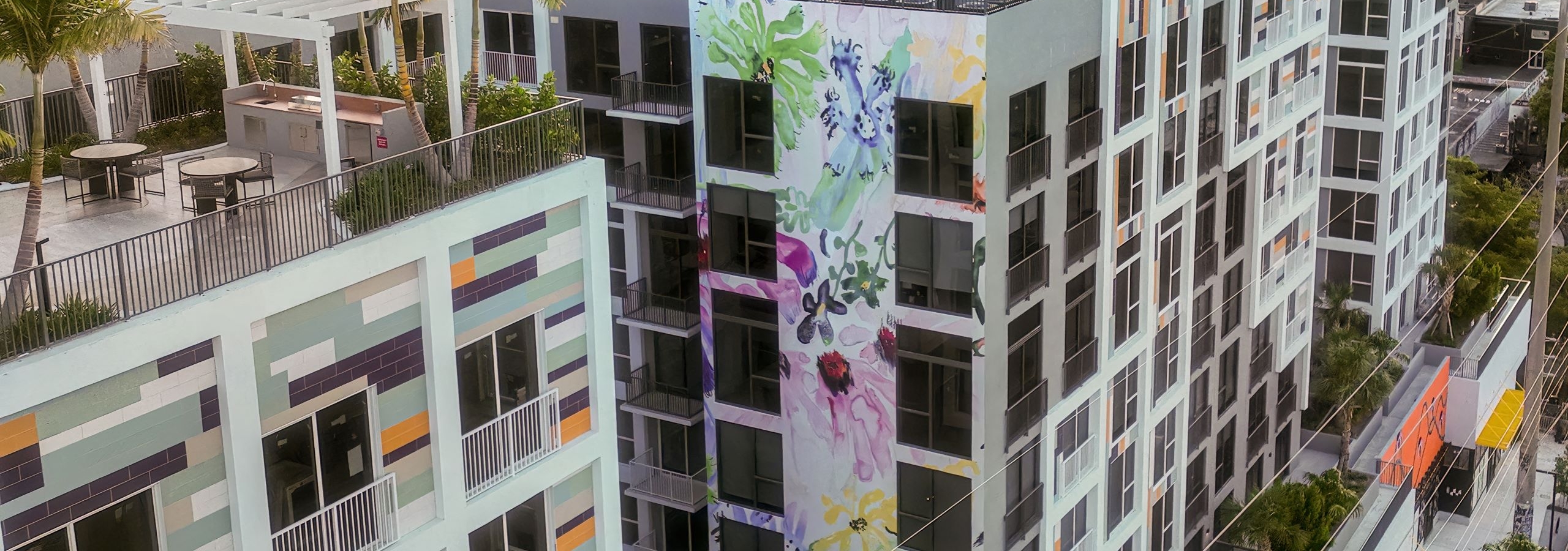 An aerial view of AMLI Wynwood apartment building adorned with a colorful floral mural with skyline in the distance