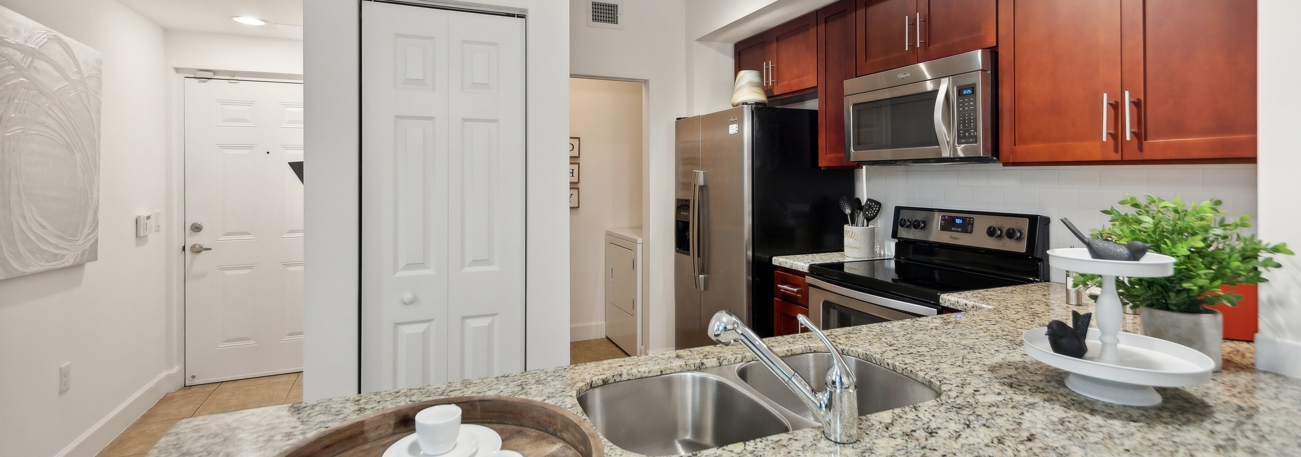 Open kitchen at AMLI Toscana Place apartments with a granite counter and stainless steel appliances set into cherry cabinets