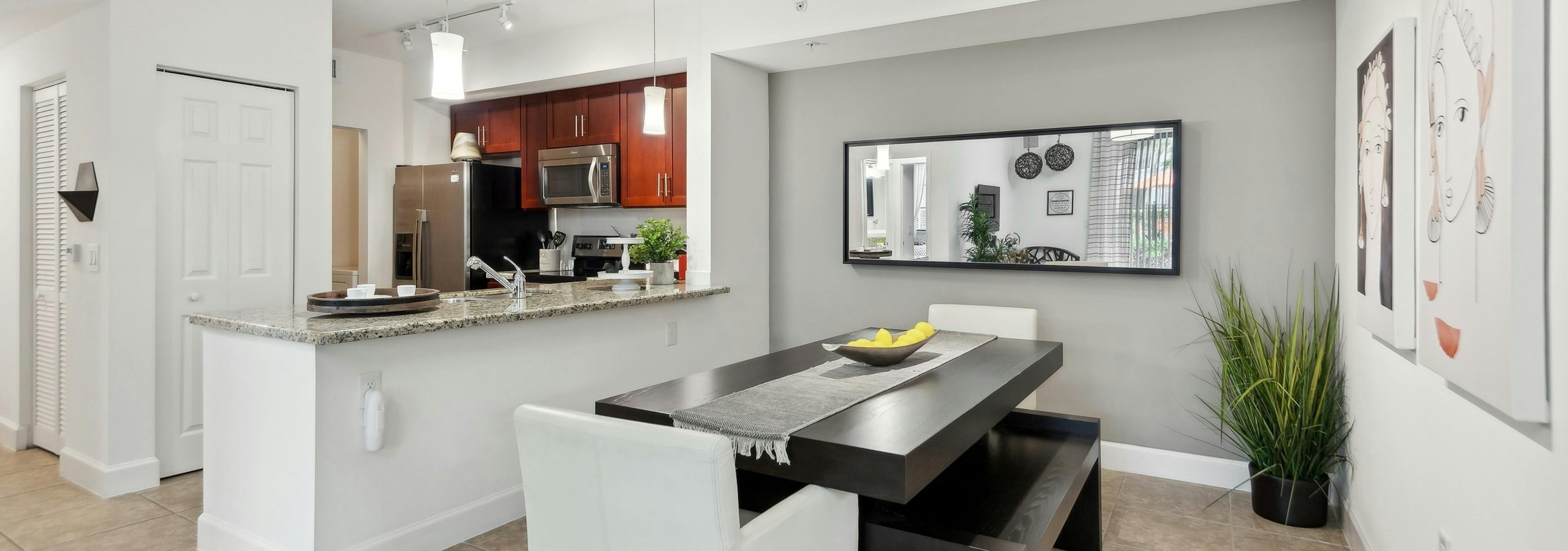 Dining room at AMLI Toscana Place apartments with a dining table looking into a kitchen with cherry cabinets and stainless steel appliances