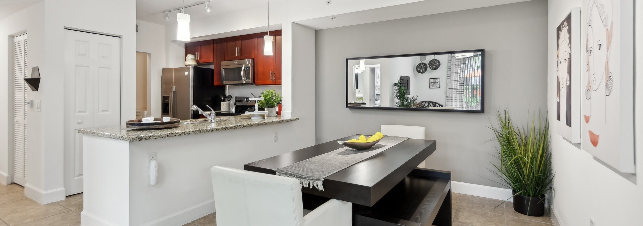 Dining room at AMLI Toscana Place apartments with a dining table looking into a kitchen with cherry cabinets and stainless steel appliances