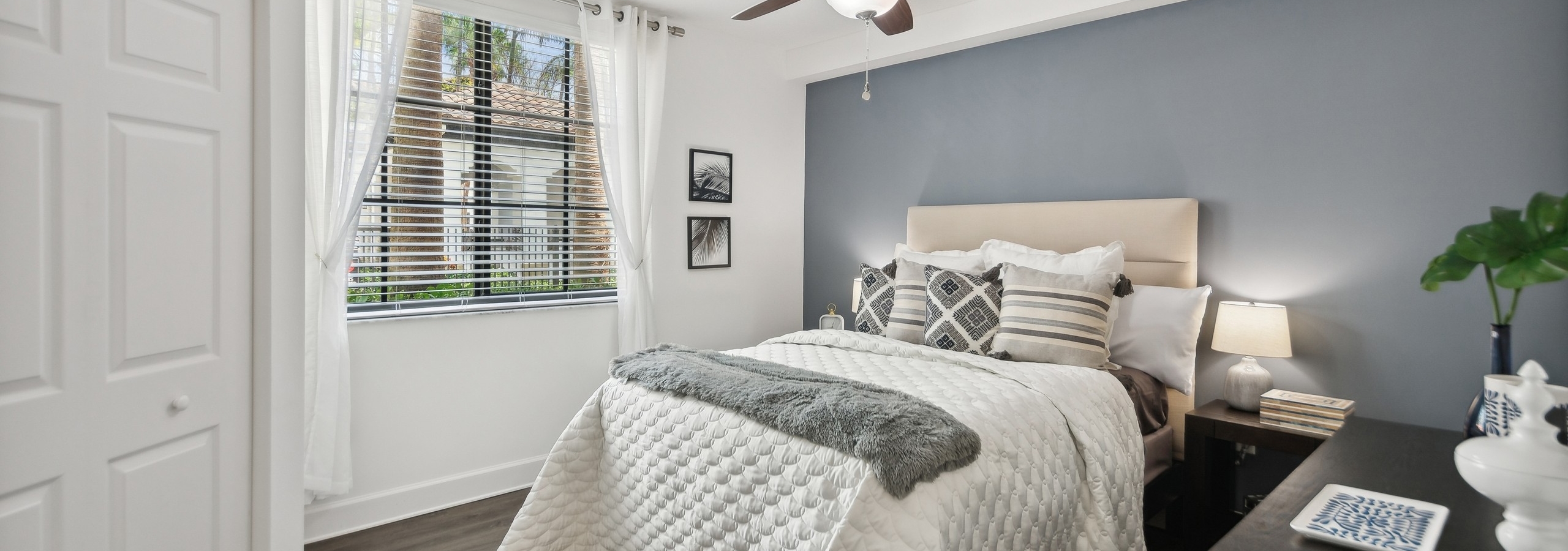 AMLI Toscana Place apartment bedroom with a queen bed and night stand on a gray accent wall and a window with white curtains