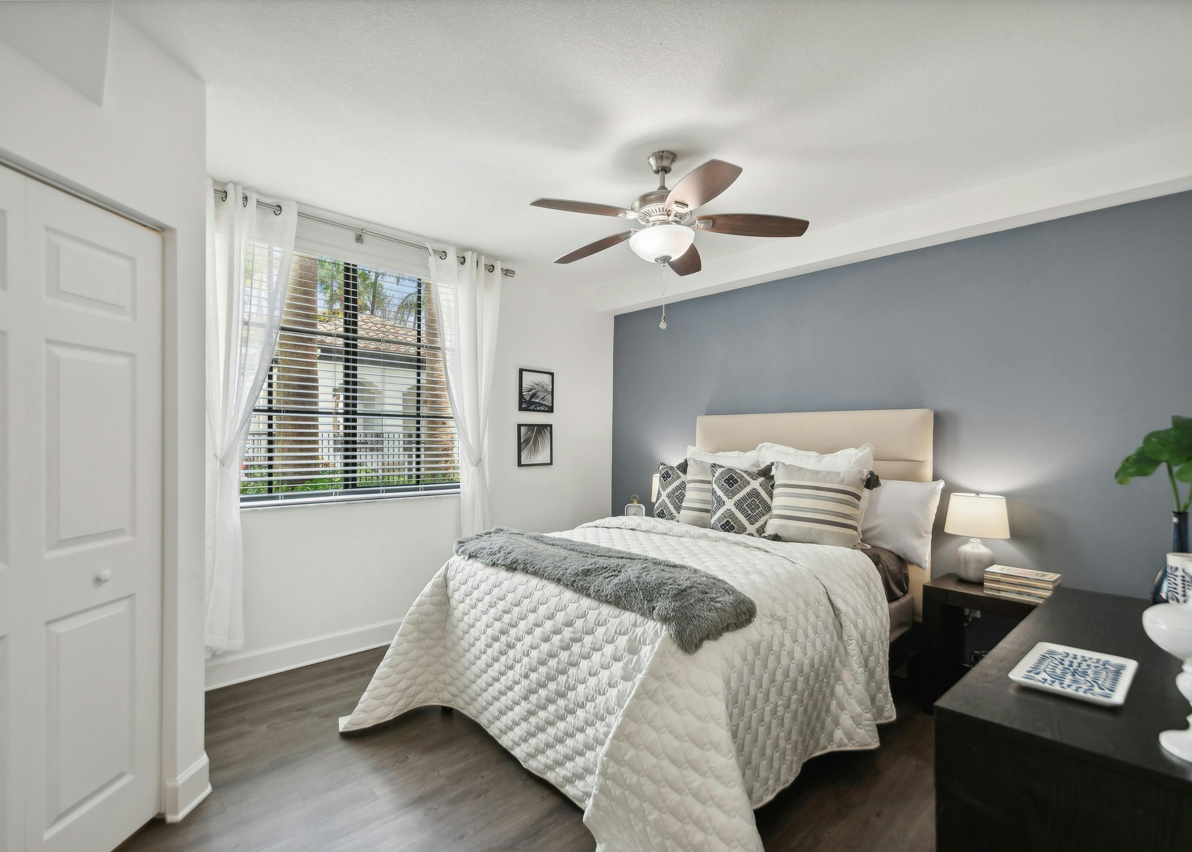 AMLI Toscana Place apartment bedroom with a queen bed and night stand on a gray accent wall and a window with white curtains
