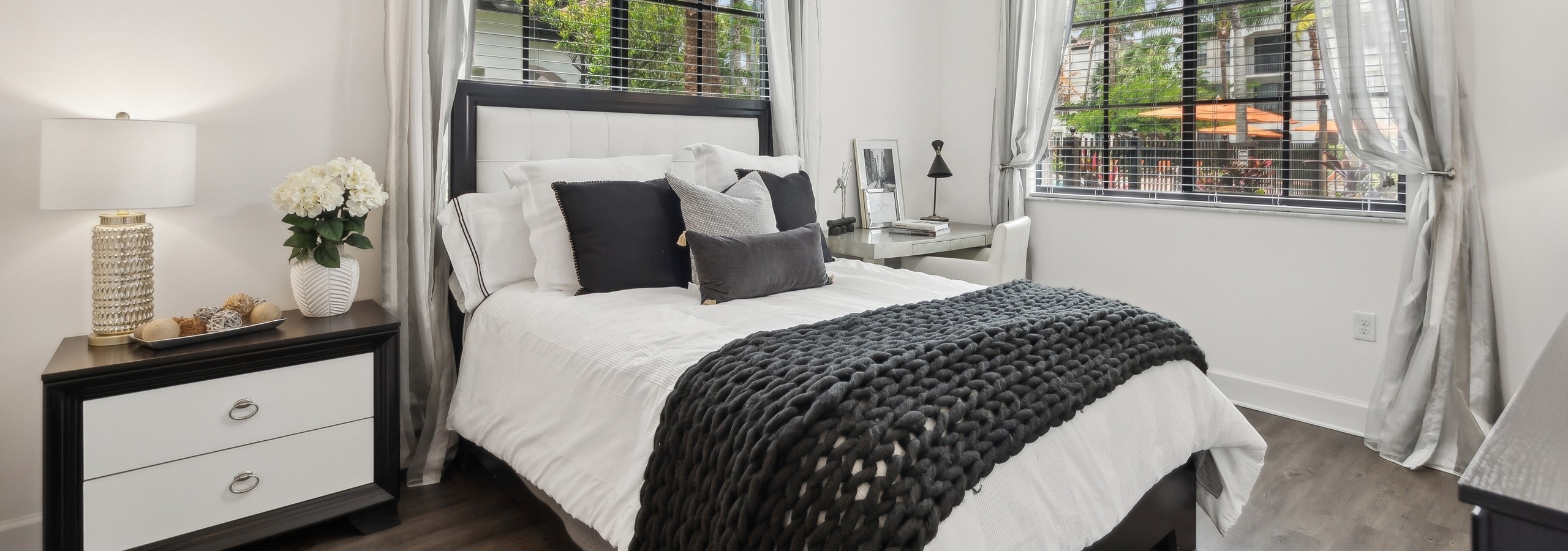 Large bedroom at AMLI Toscana Place apartments with queen bed and nightstand below two windows with gray curtains