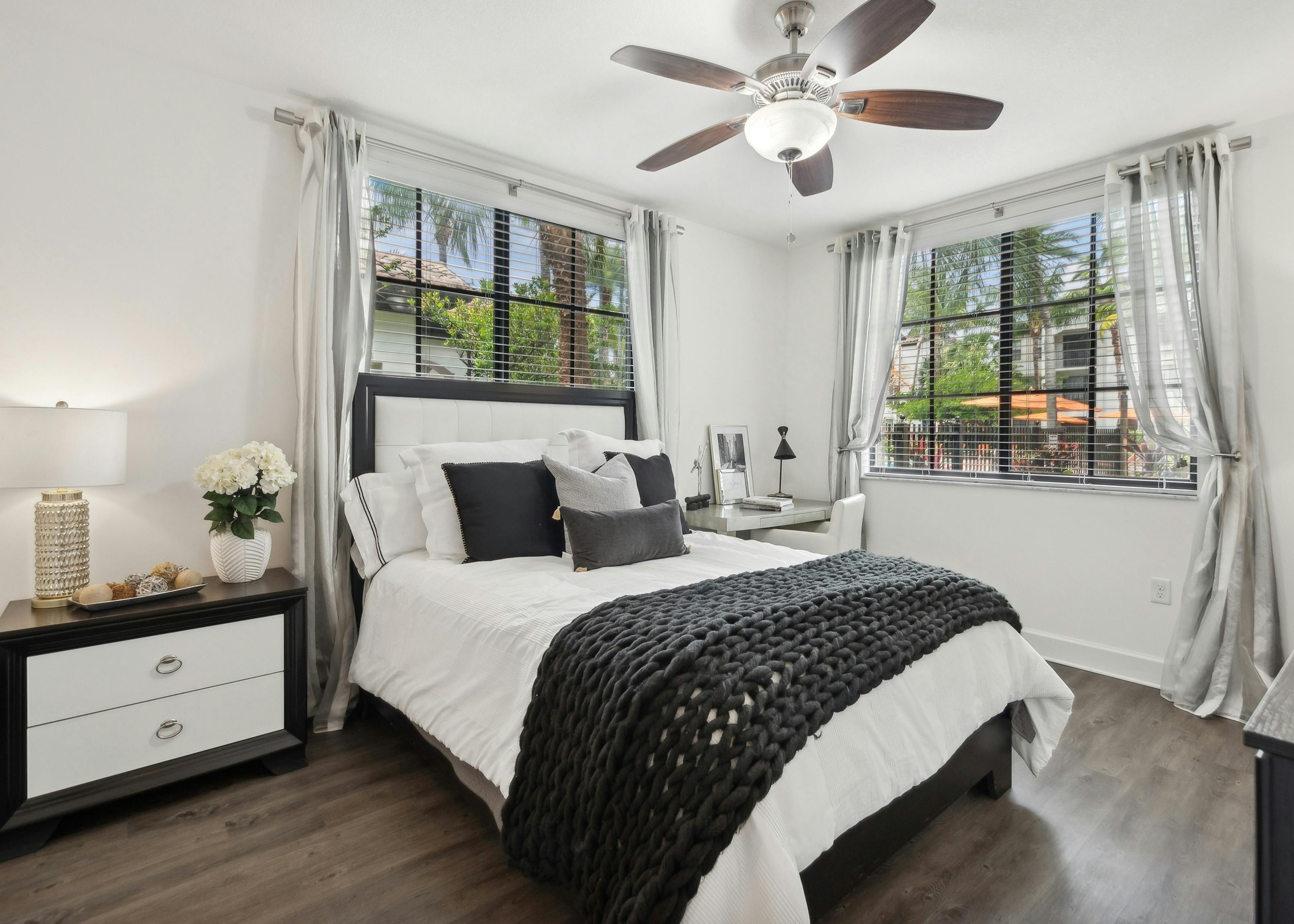 Large bedroom at AMLI Toscana Place apartments with queen bed and nightstand below two windows with gray curtains