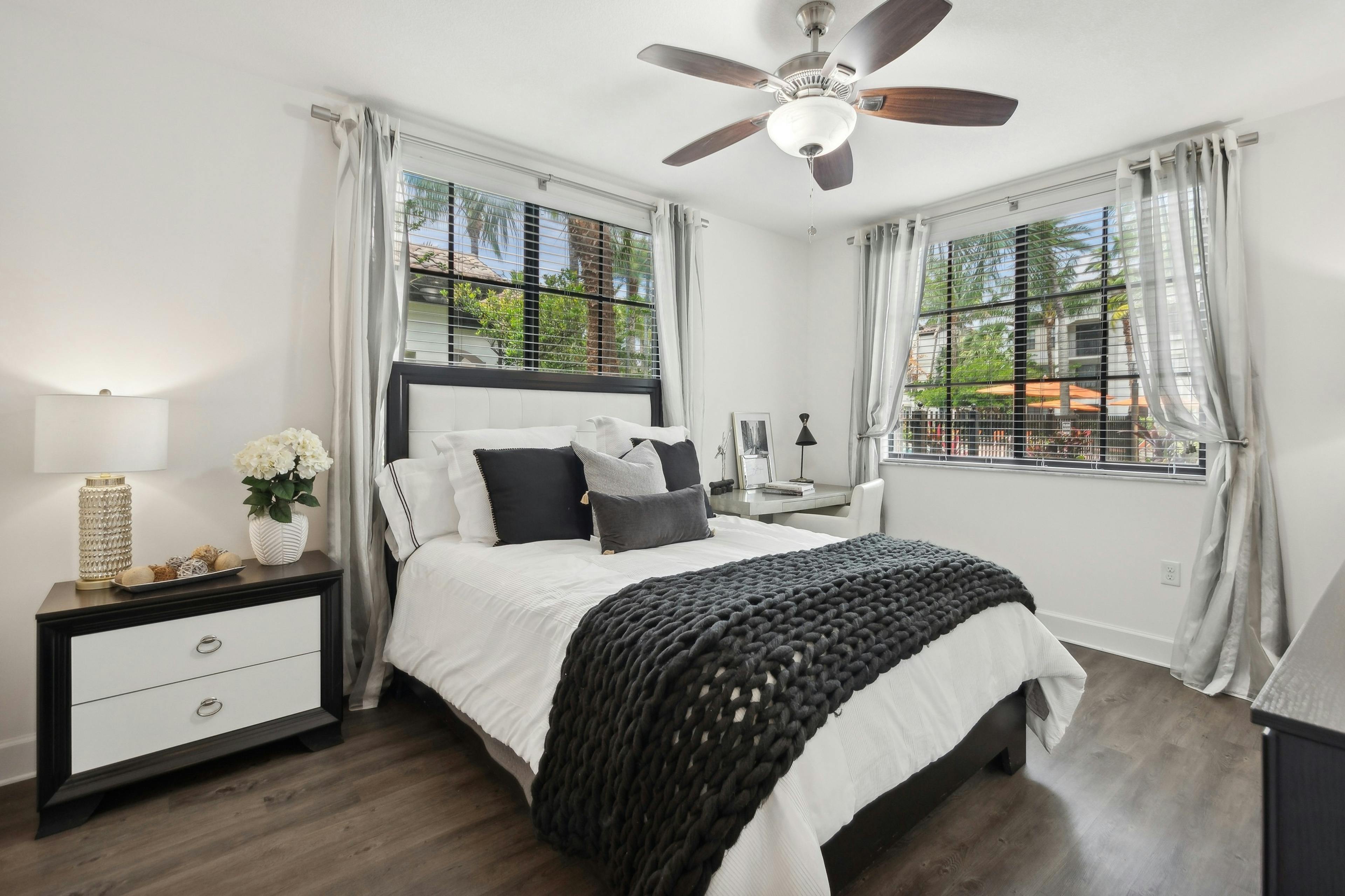 Large bedroom at AMLI Toscana Place apartments with queen bed and nightstand below two windows with gray curtains