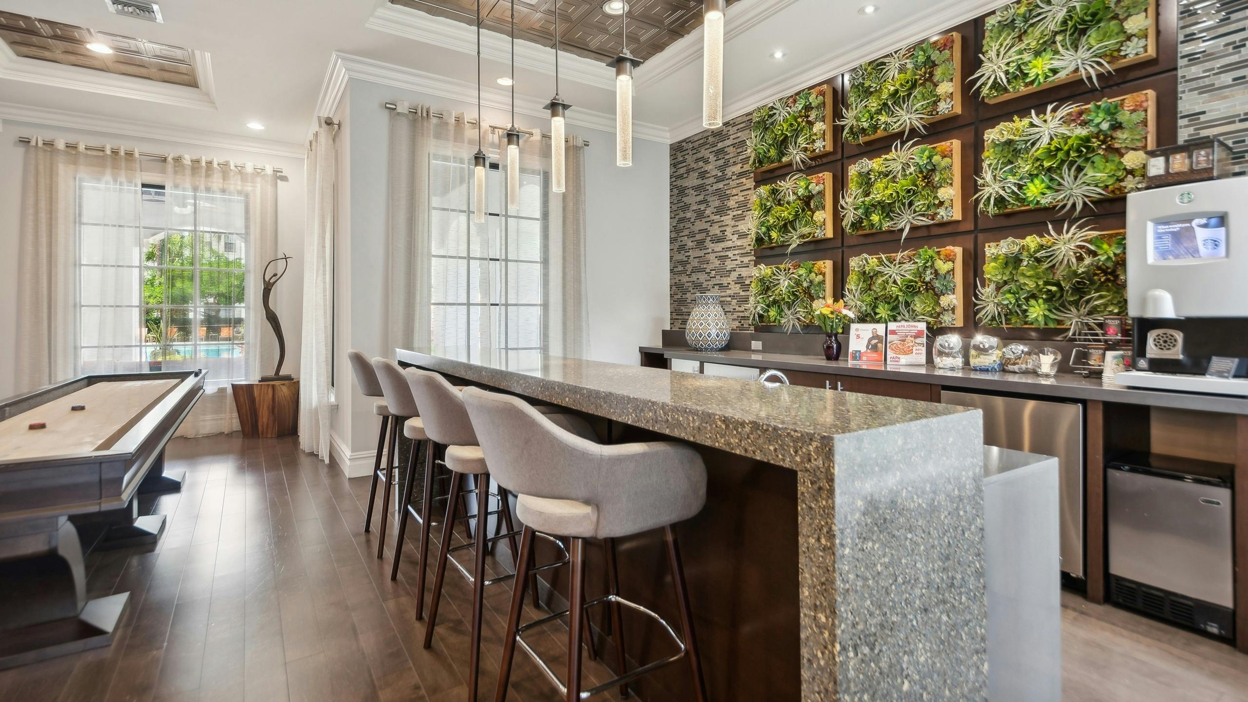Resident lounge coffee bar with 4 stools and a coffee machine on a waterfall countertop next to a shuffleboard table at AMLI Toscana Place