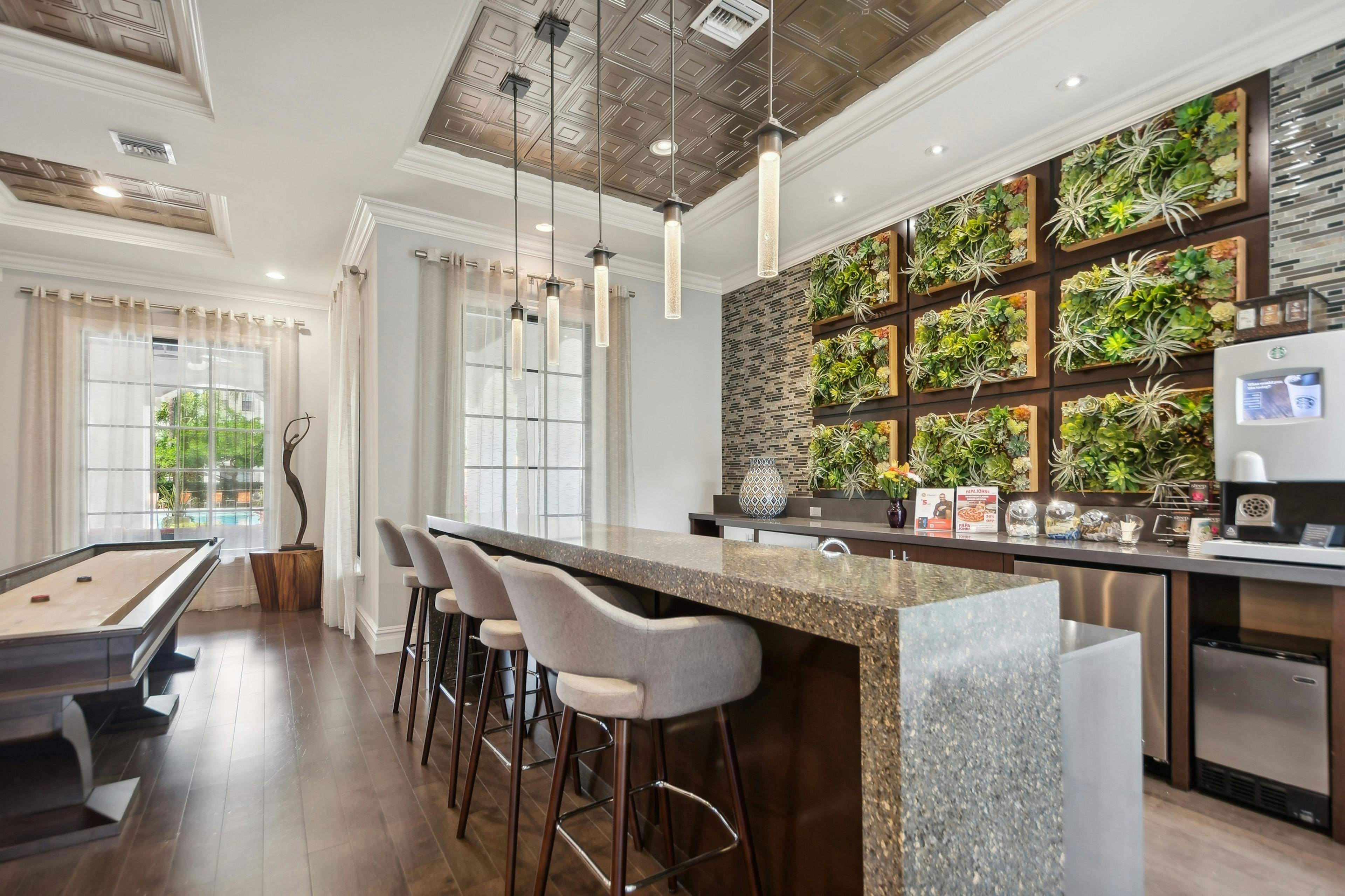 Resident lounge coffee bar with 4 stools and a coffee machine on a waterfall countertop next to a shuffleboard table at AMLI Toscana Place
