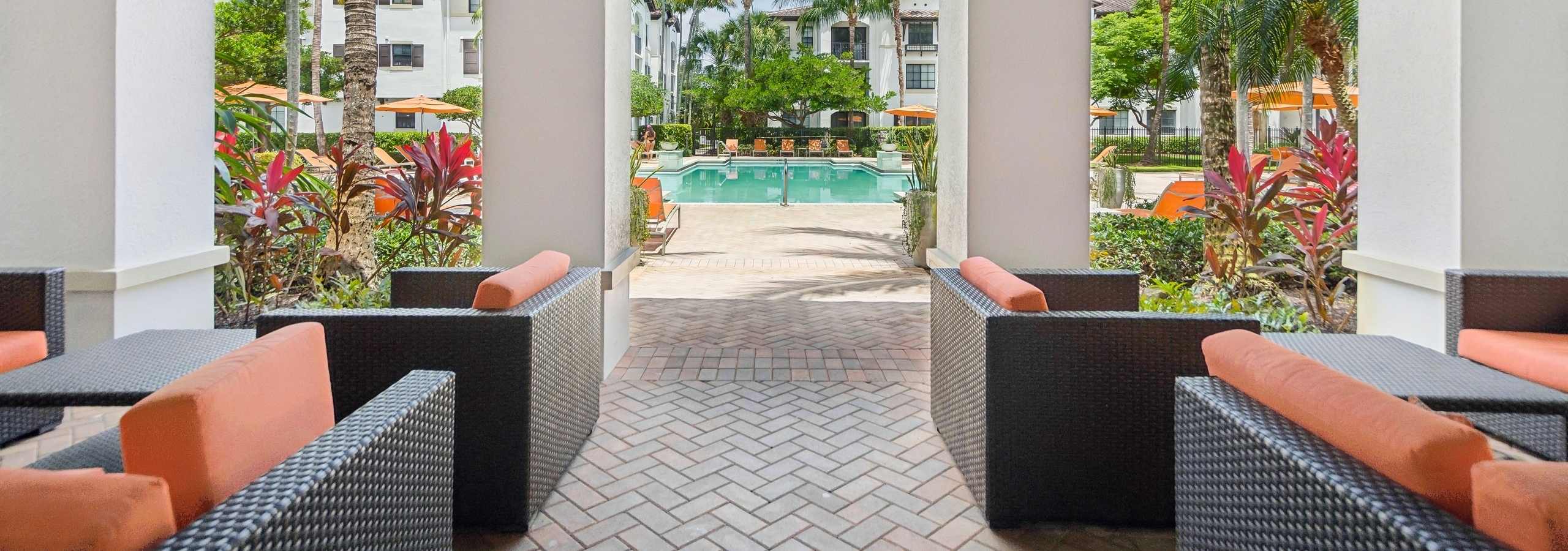 A covered patio with outdoor seating at AMLI Toscana place apartments looking out at a swimming pool surrounded by lounge chairs