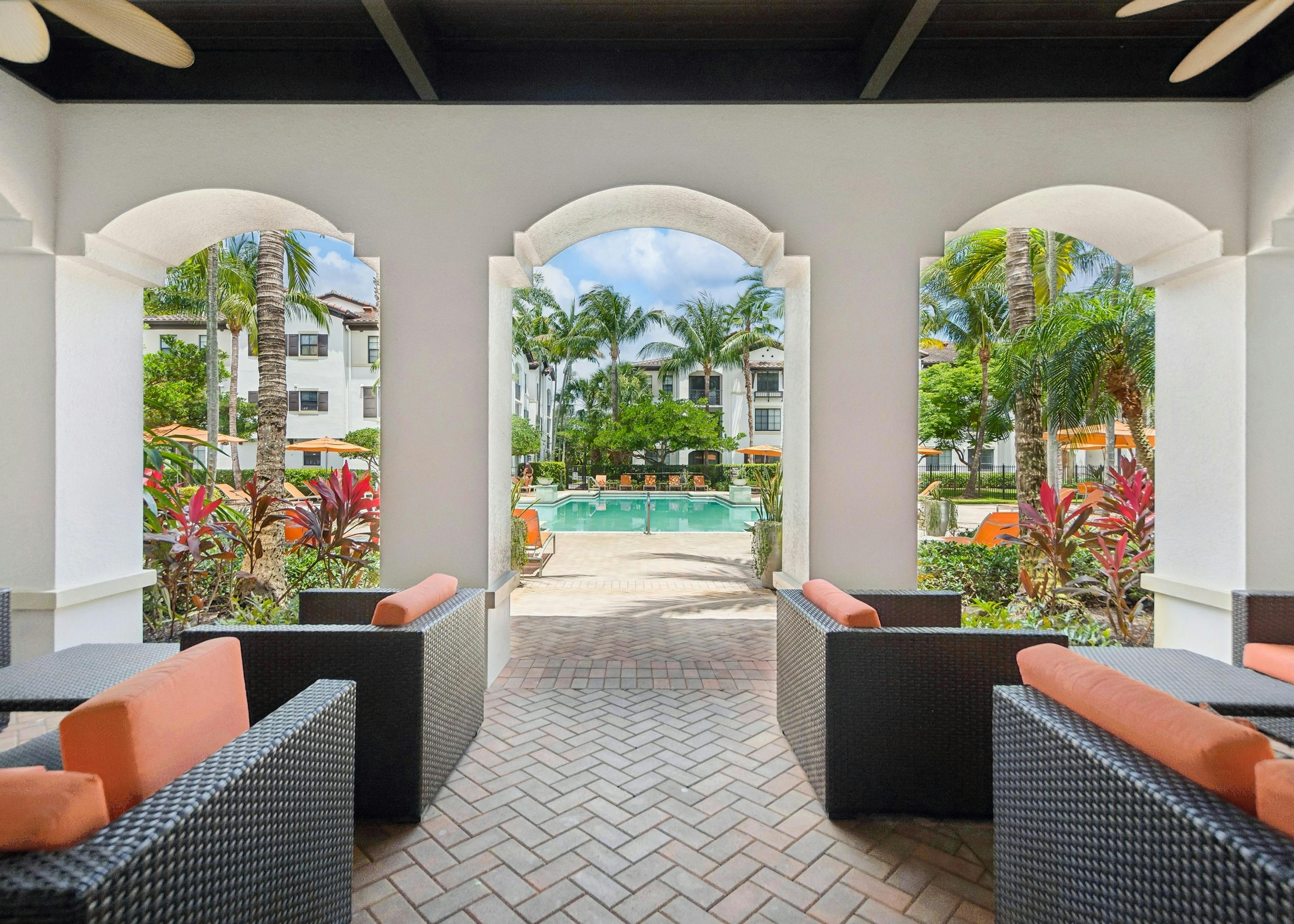 A covered patio with outdoor seating at AMLI Toscana place apartments looking out at a swimming pool surrounded by lounge chairs