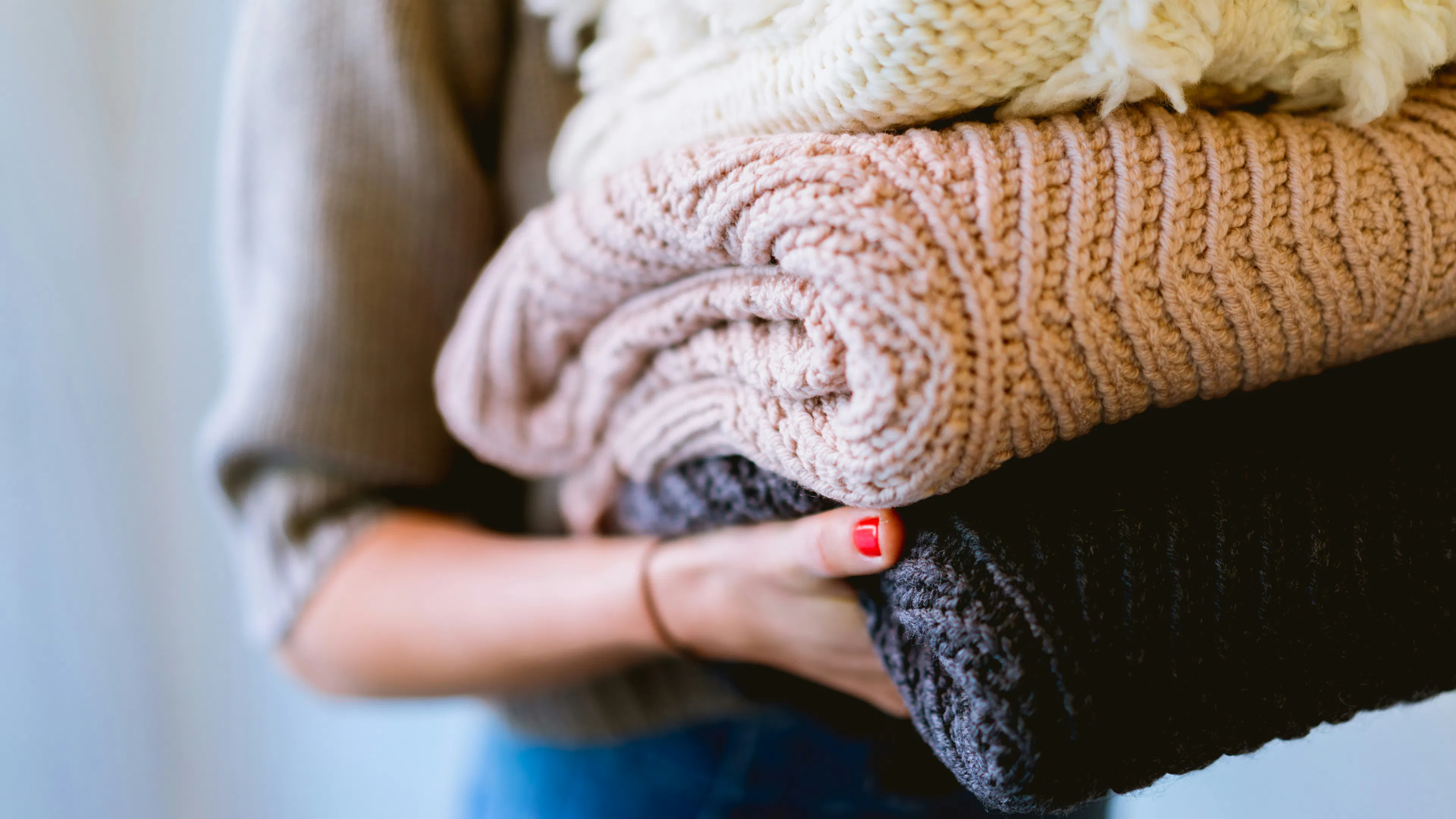 A woman holding three folded wool sweaters in her arms
