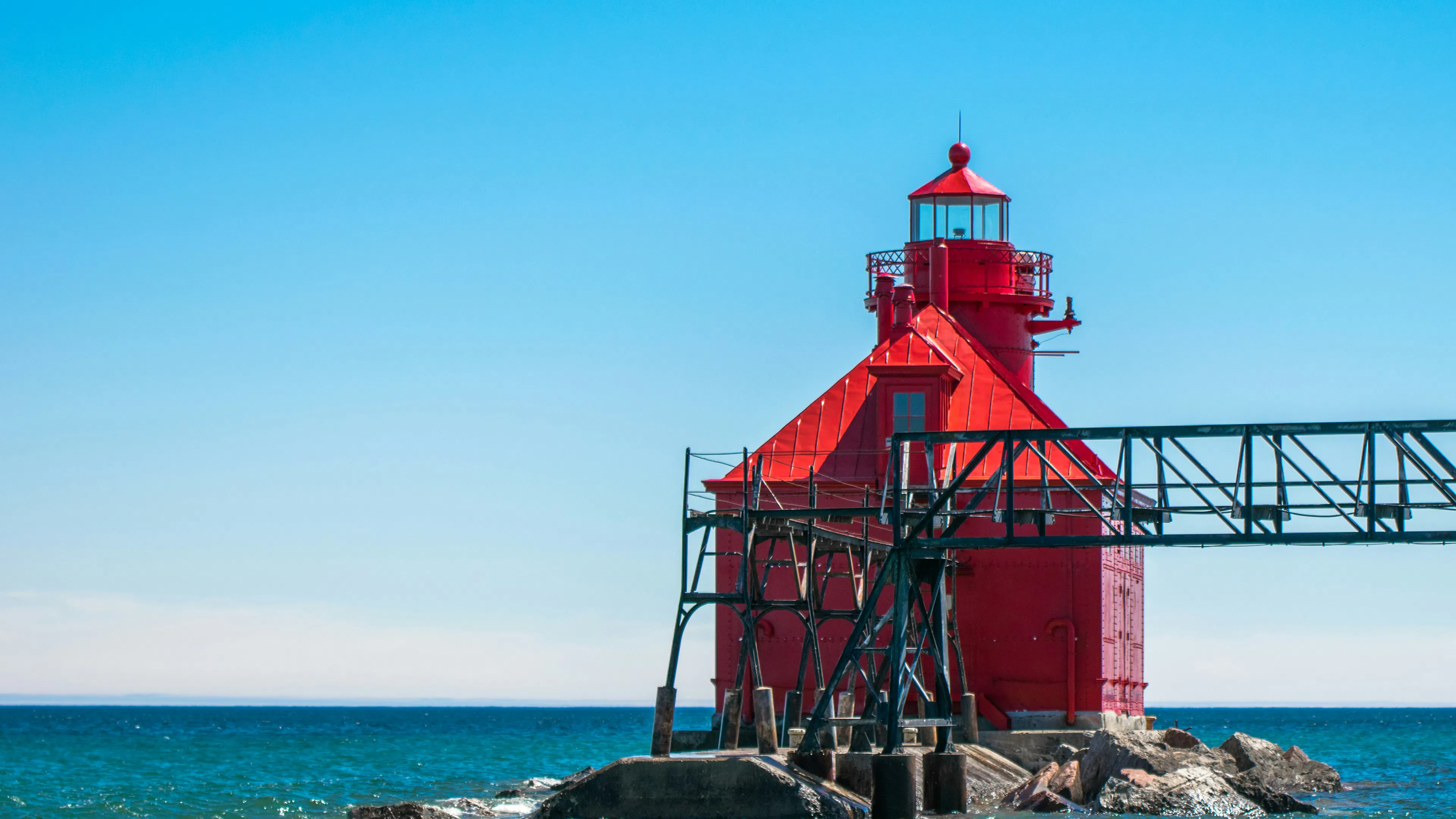 The bright red exterior of the small Sturgeon Bay Pierhead Lighthouse seen on a clear day against the water