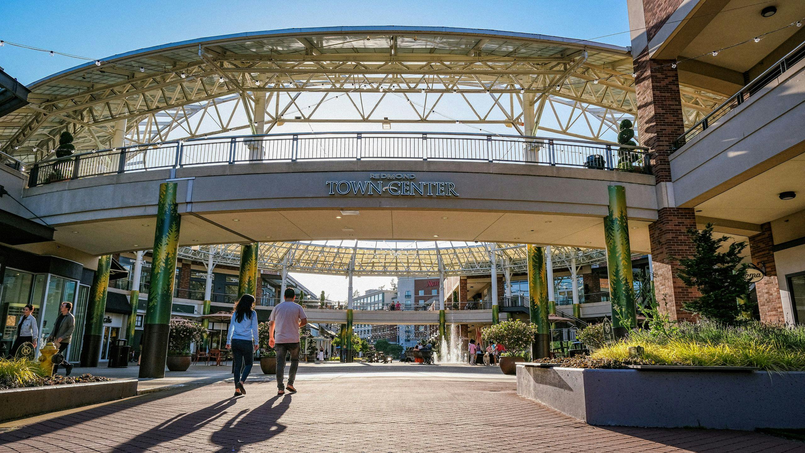 Photos of a couple walking under a bridge into the Redmond Town Center with blue skies above