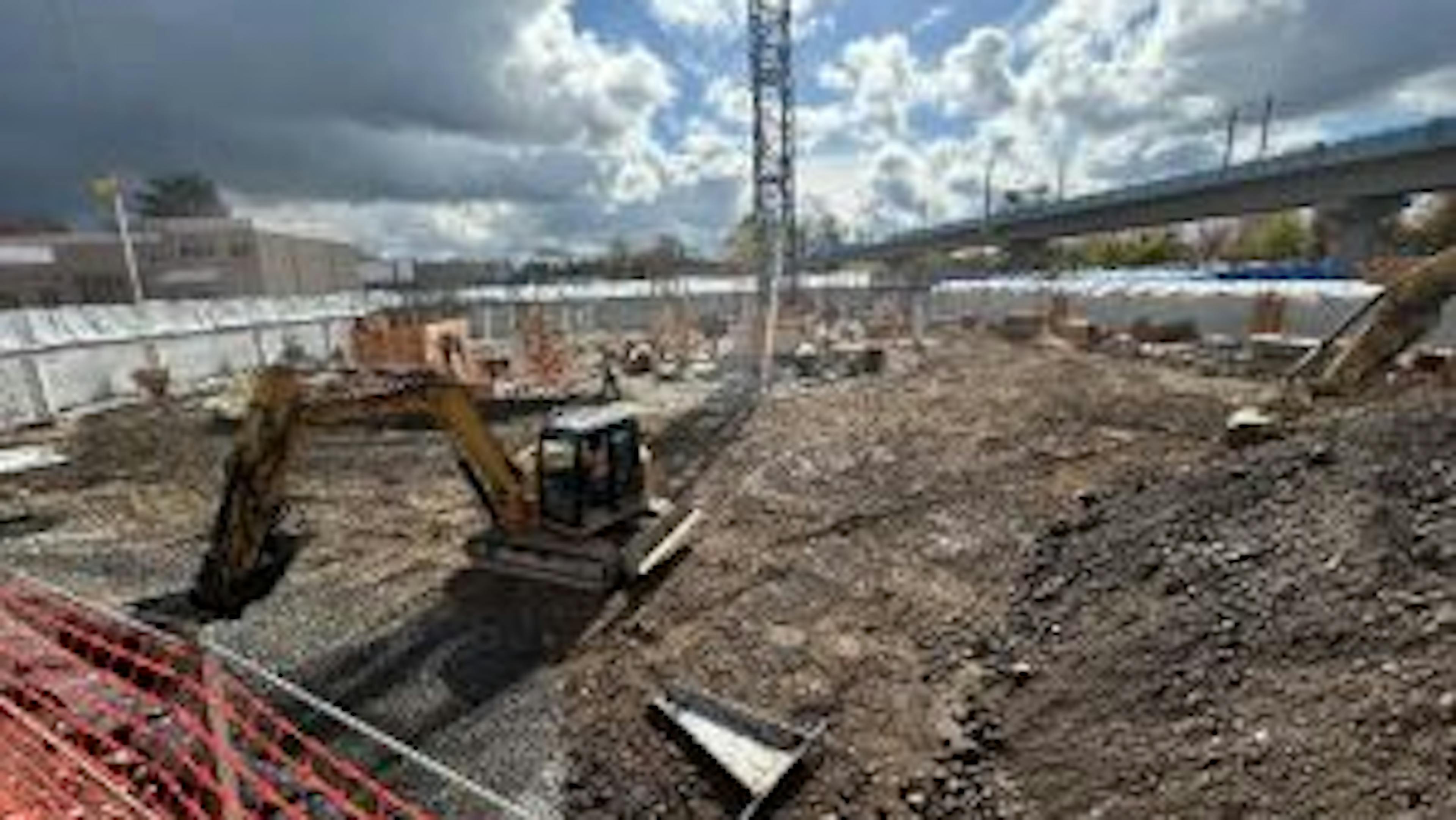 Daytime view of AMLI Redmond Way construction site with large excavator moving dirt and orange fencing