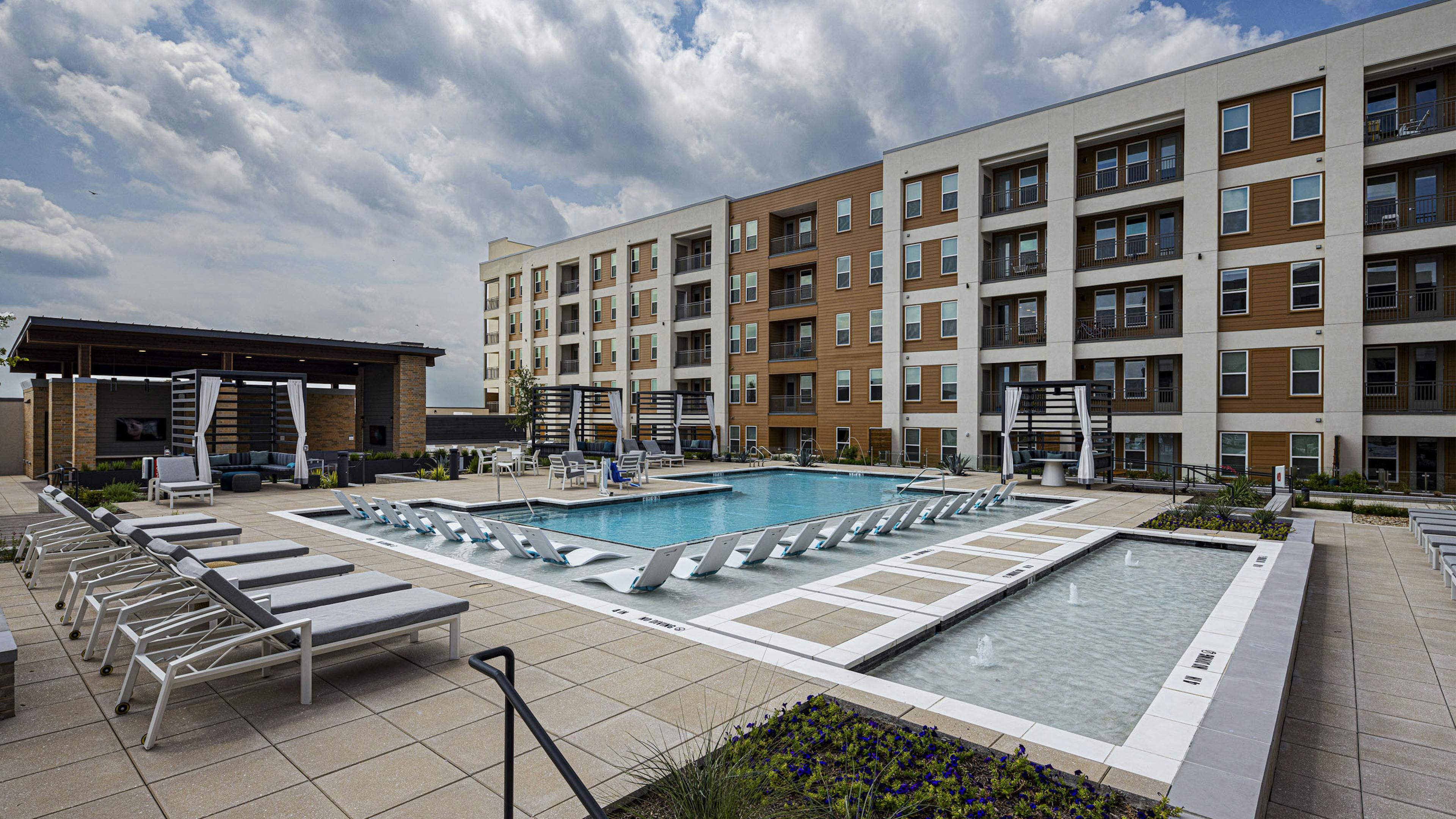 AMLI Branch Park apartment building overlooking a large outdoor pool area with cabanas, gray and white lounge chairs and submerged white loungers