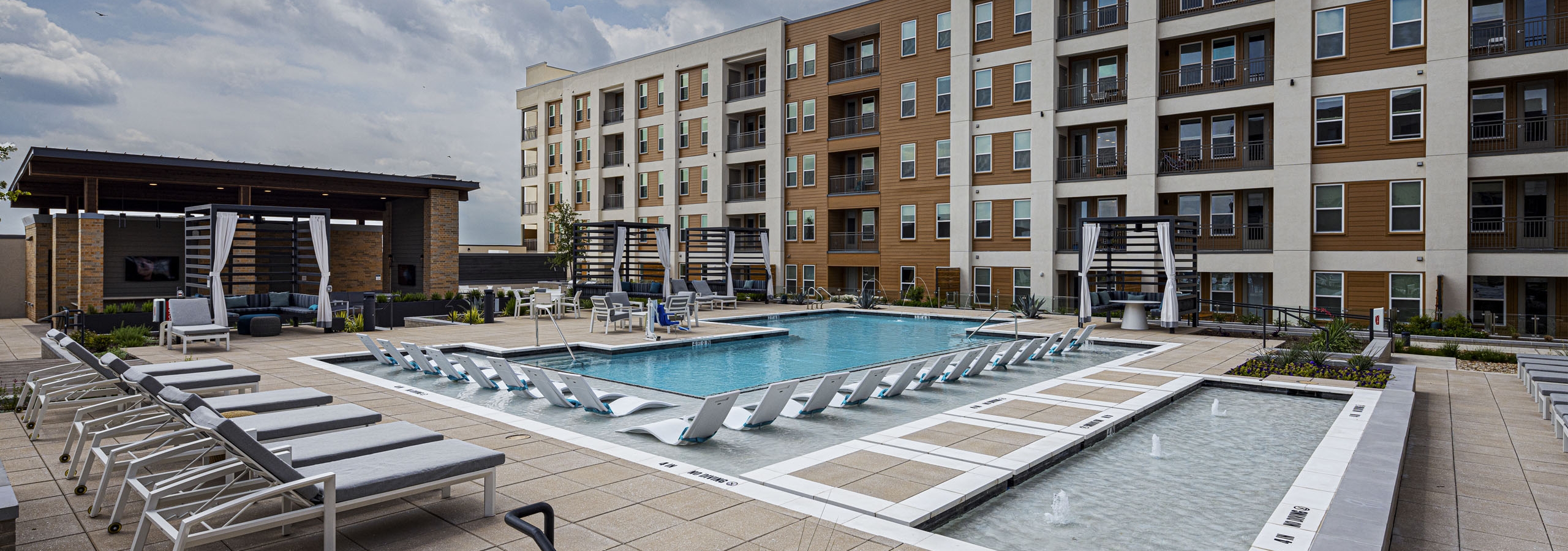 AMLI Branch Park apartment building overlooking a large outdoor pool area with cabanas, gray and white lounge chairs and submerged white loungers