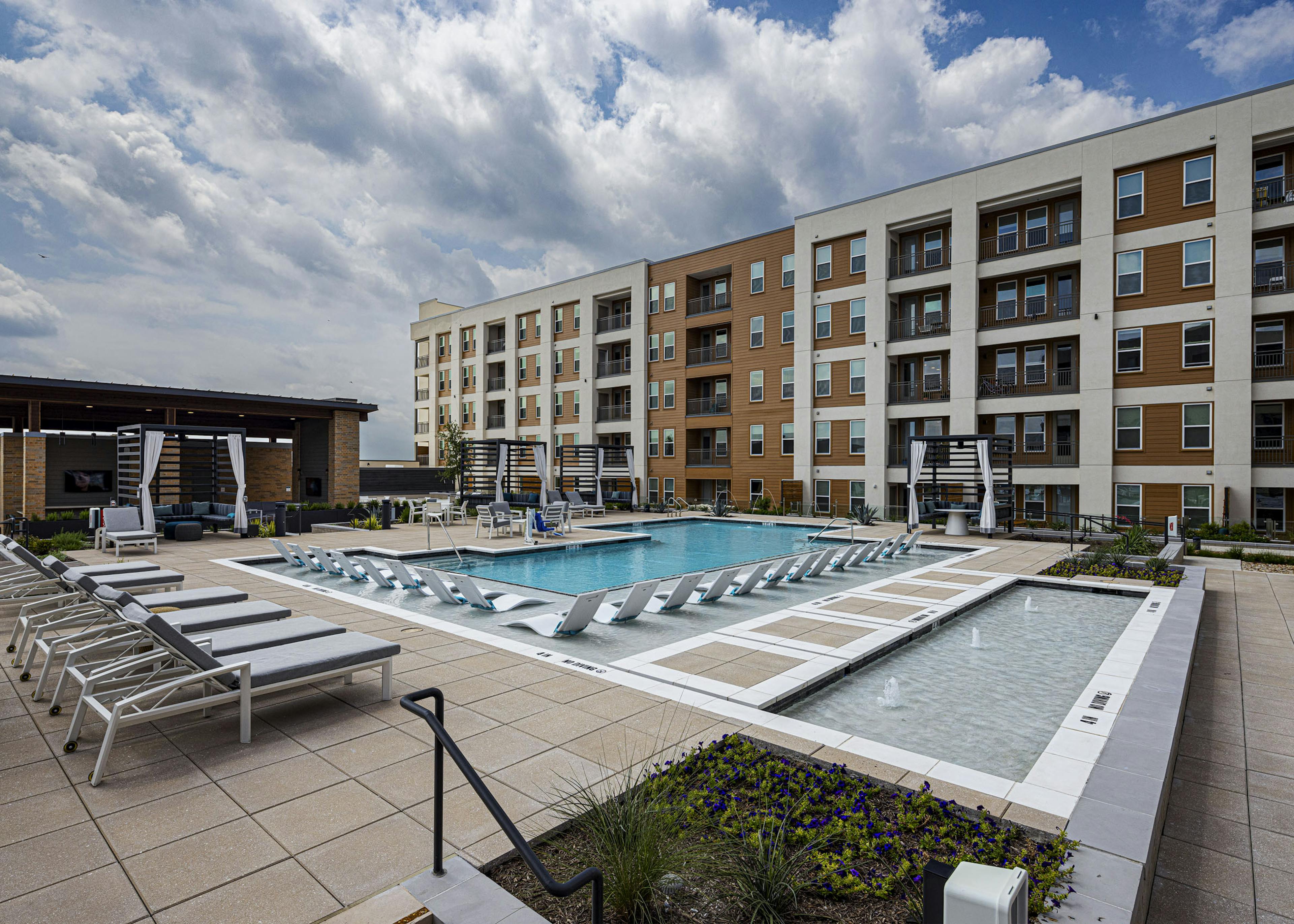 AMLI Branch Park apartment building overlooking a large outdoor pool area with cabanas, gray and white lounge chairs and submerged white loungers