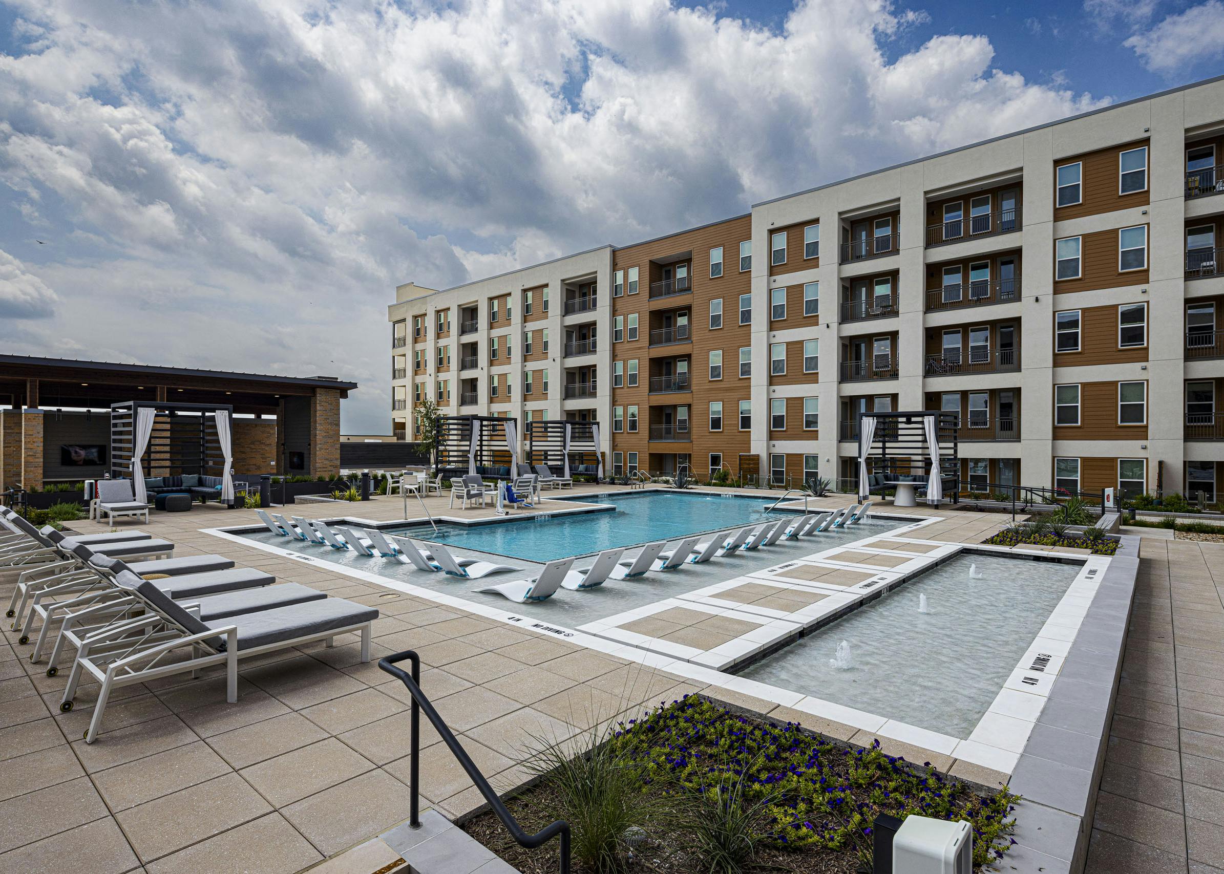 AMLI Branch Park apartment building overlooking a large outdoor pool area with cabanas, gray and white lounge chairs and submerged white loungers