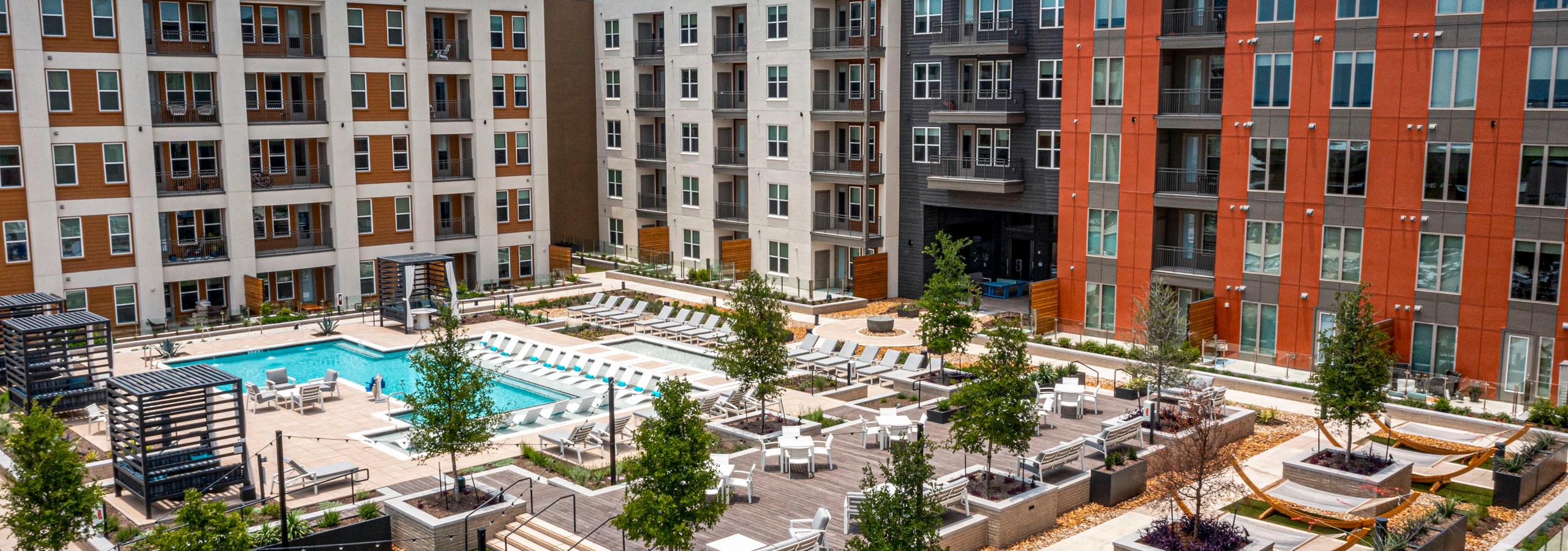 Aerial view of AMLI Branch Park apartments courtyard featuring a large pool, sun loungers, cabanas, tree planters and greenery