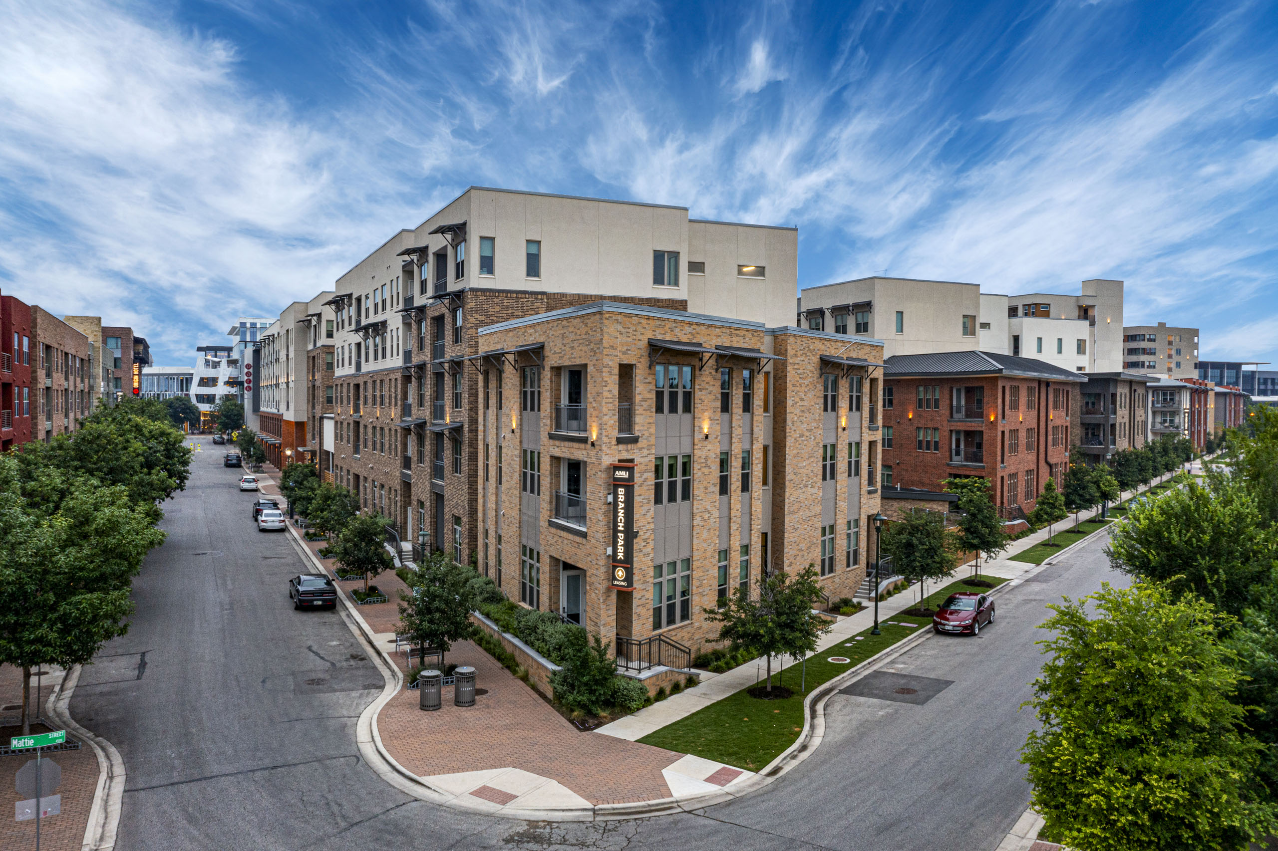 Daytime street corner view of AMLI Branch Park apartment building exterior featuring tan brick walls and deep blue sky above