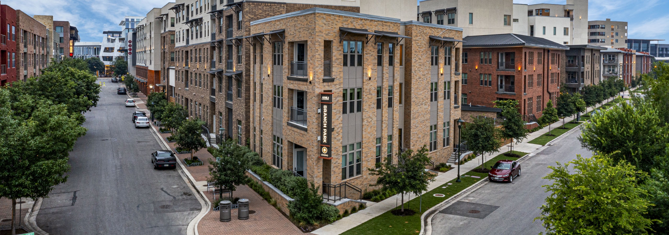 Daytime street corner view of AMLI Branch Park apartment building exterior featuring tan brick walls and deep blue sky above