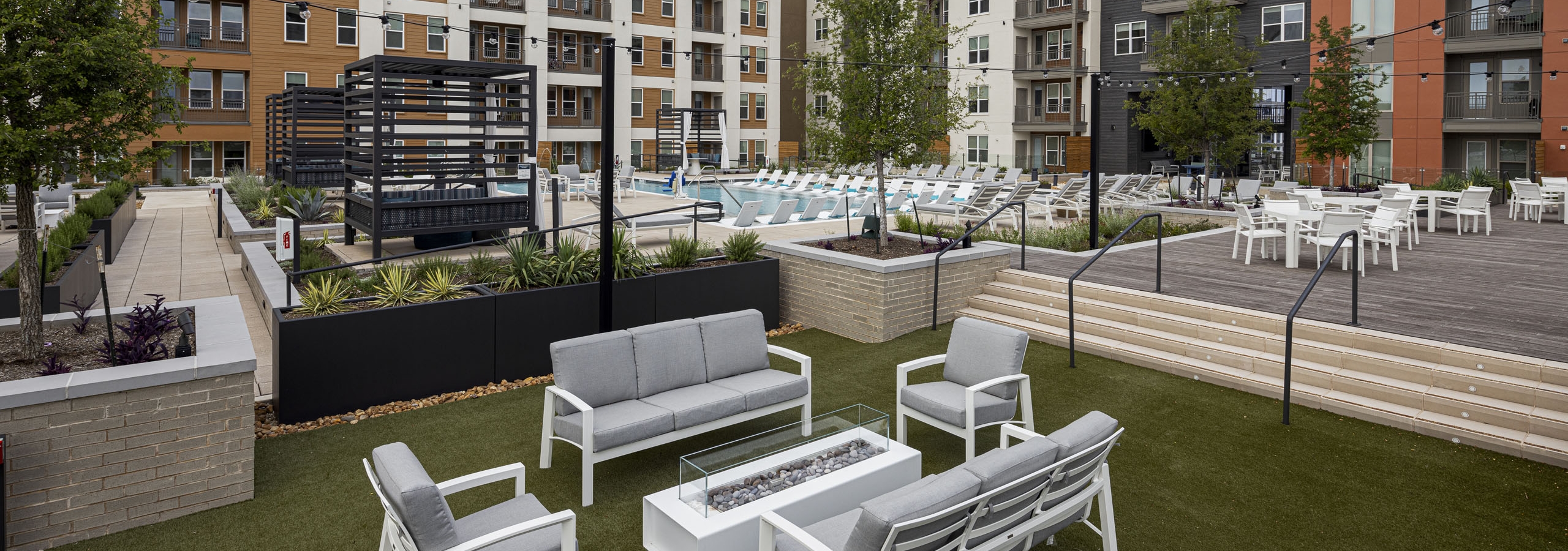 Resident courtyard at AMLI Branch Park featuring seating surrounding a firepit on turf and a pool in the background