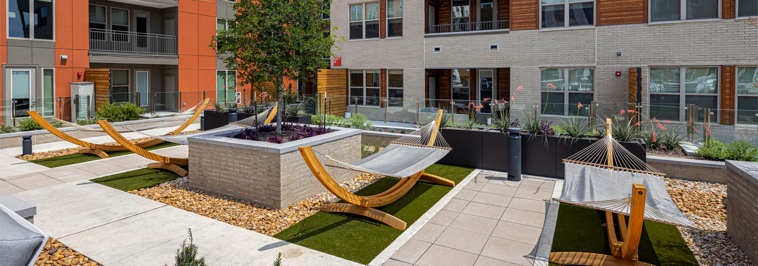 An outdoor courtyard at AMLI Branch Park apartments featuring several hammocks, green artificial turf, and a central raised garden bed.
