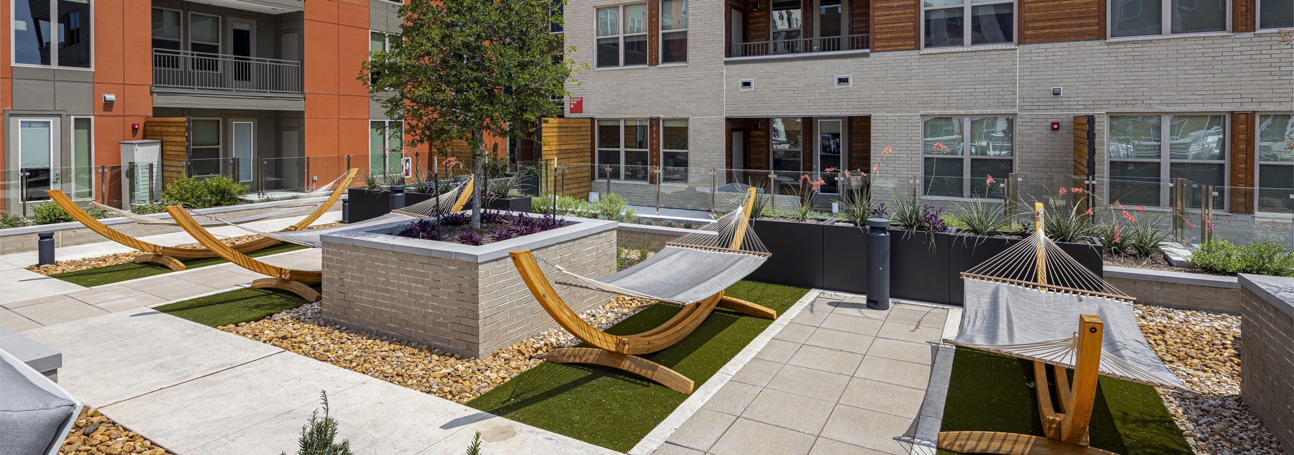 An outdoor courtyard at AMLI Branch Park apartments featuring several hammocks, green artificial turf, and a central raised garden bed.