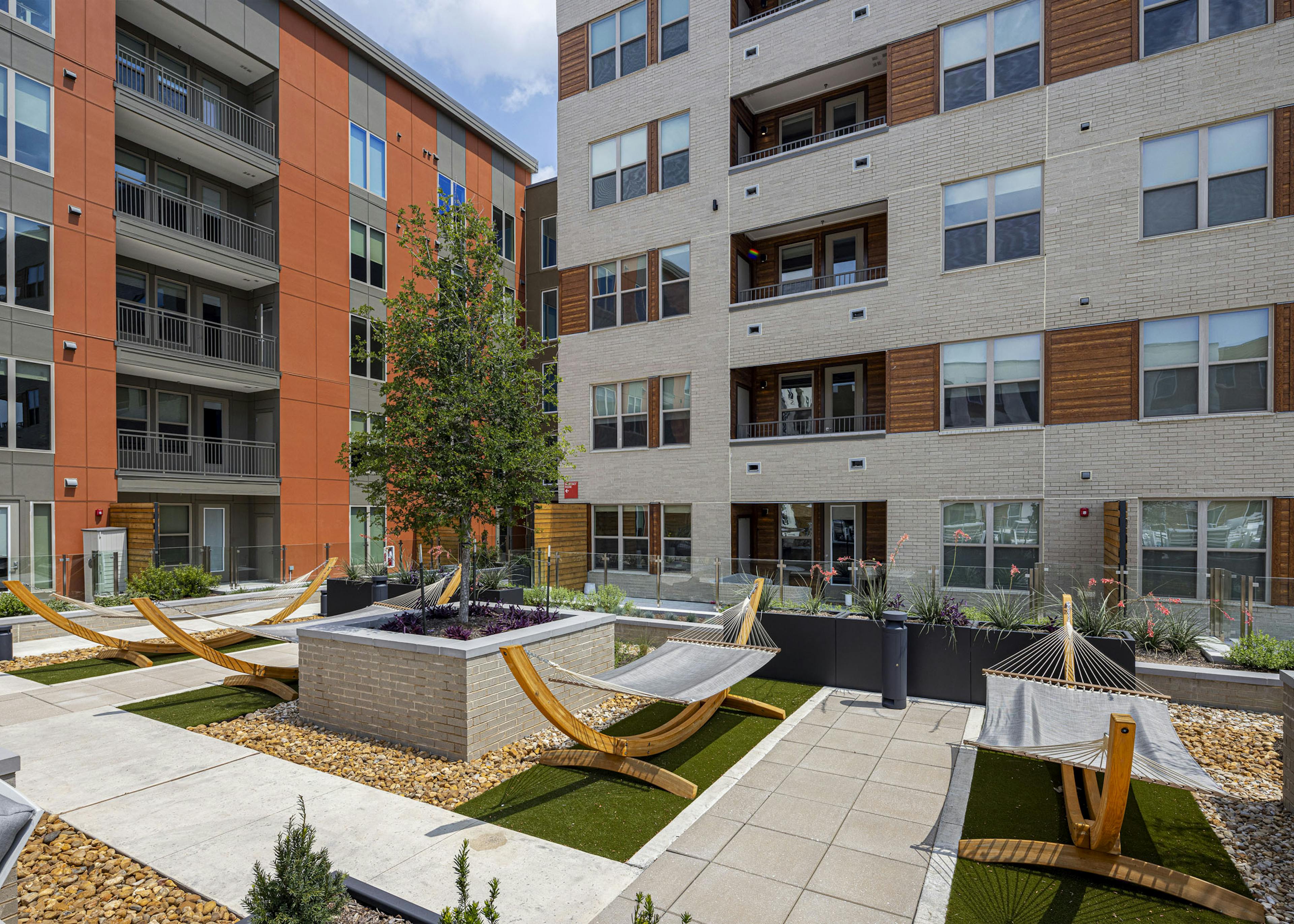 An outdoor courtyard at AMLI Branch Park apartments featuring several hammocks, green artificial turf, and a central raised garden bed.