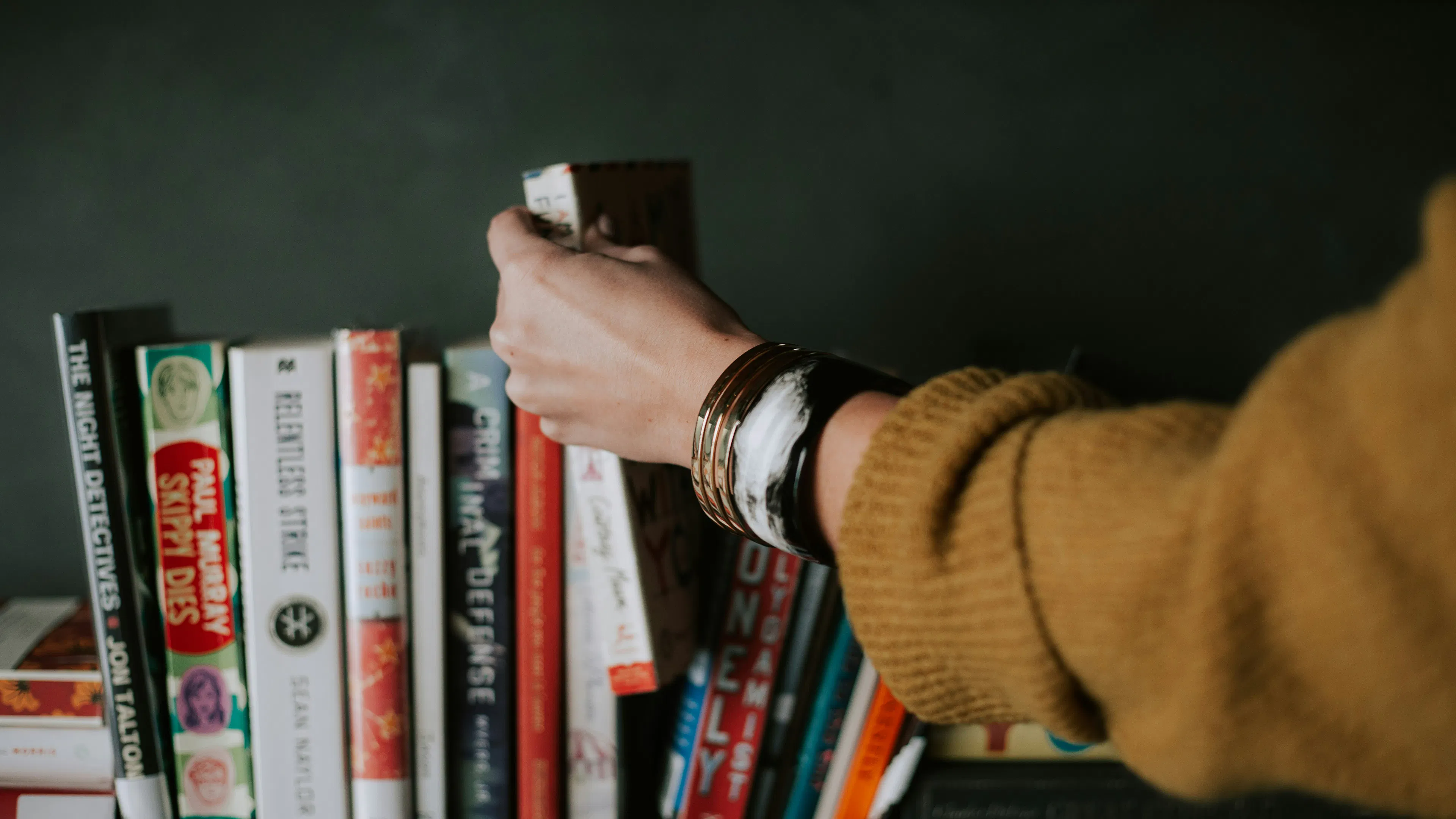 A person's hand picking up a book from a shelf full of various books