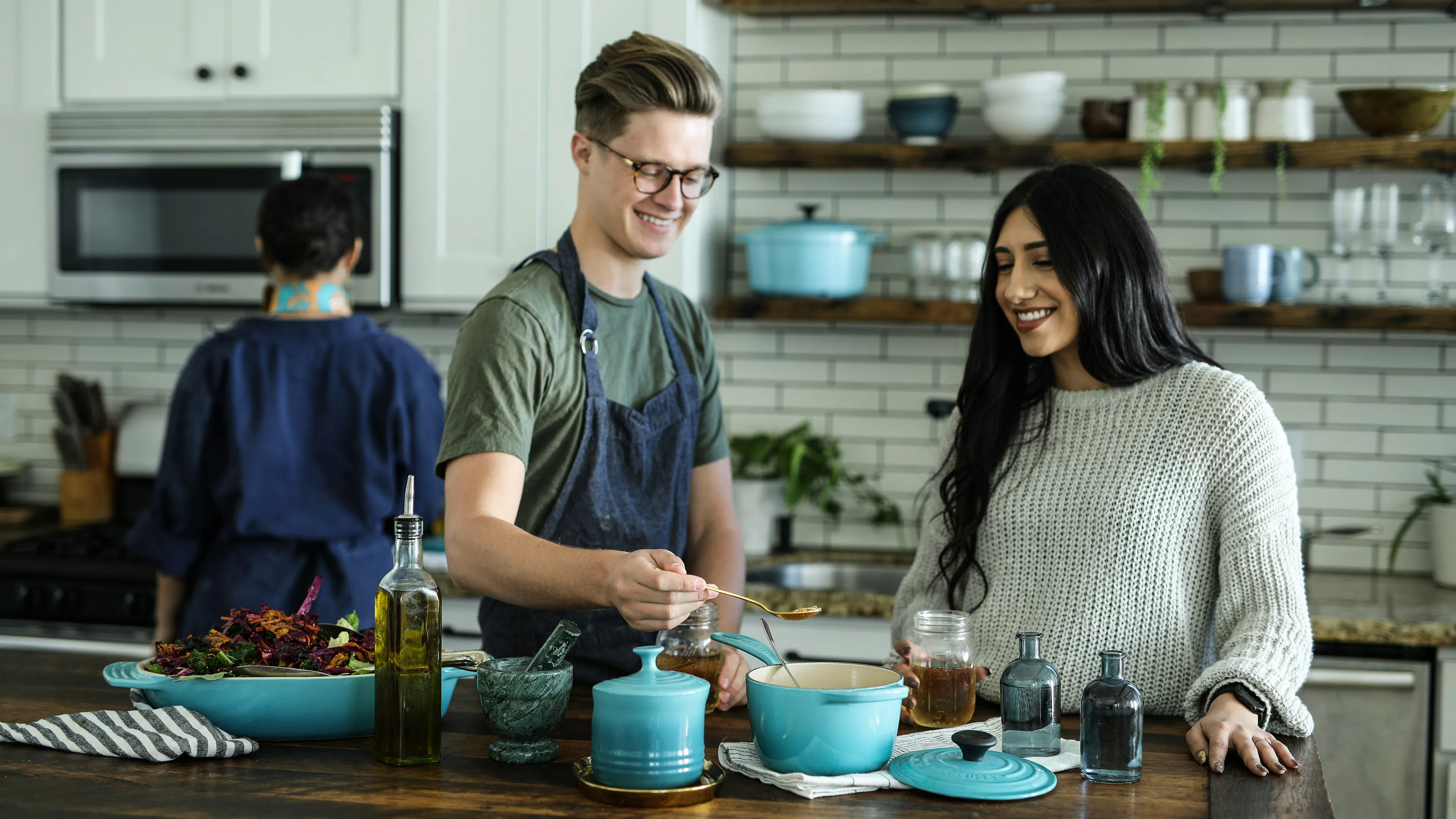 Two people cooking at a kitchen island in a modern kitchen with white subway tiles in the background