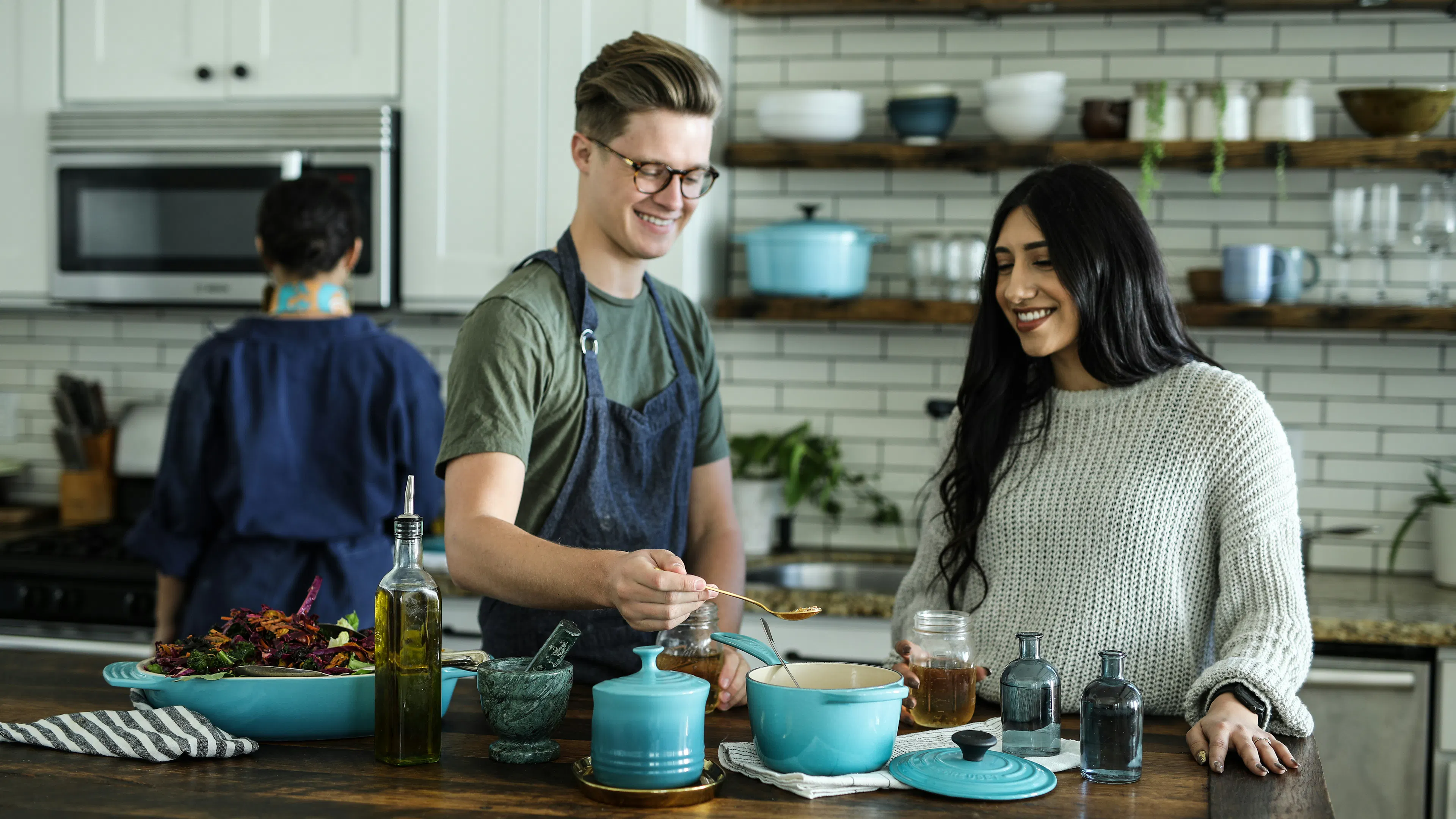 Two people cooking at a kitchen island in a modern kitchen with white subway tiles in the background