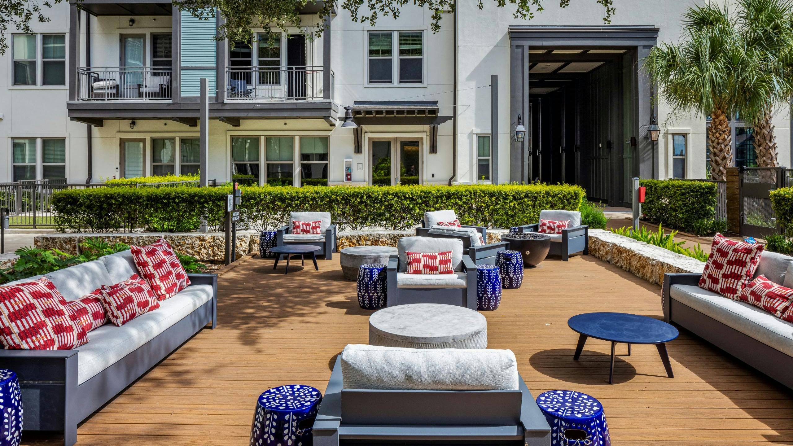 A large sunny outdoor lounge at AMLI Lakeline apartments with cushioned seating and red and white pillows and blue and white side tables