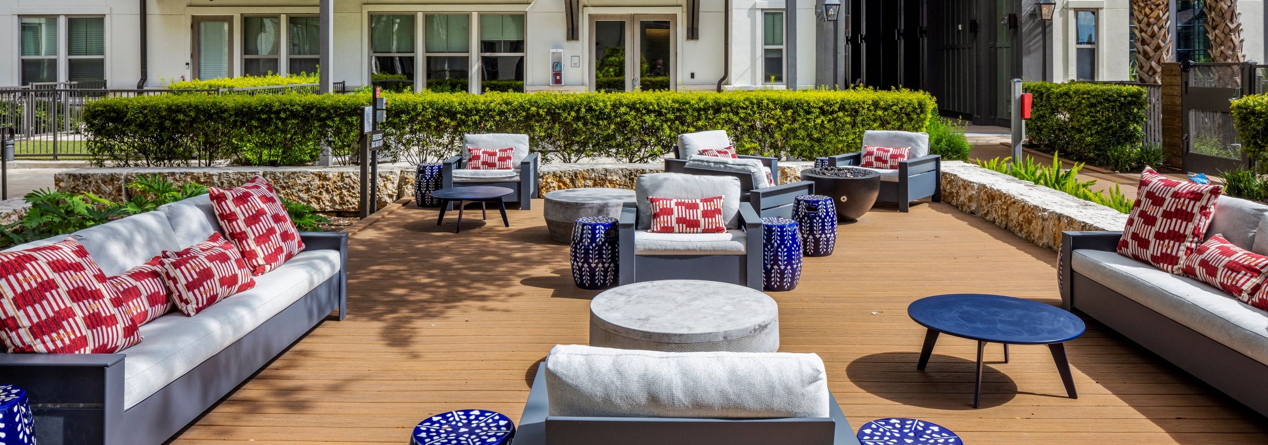 A large sunny outdoor lounge at AMLI Lakeline apartments with cushioned seating and red and white pillows and blue and white side tables