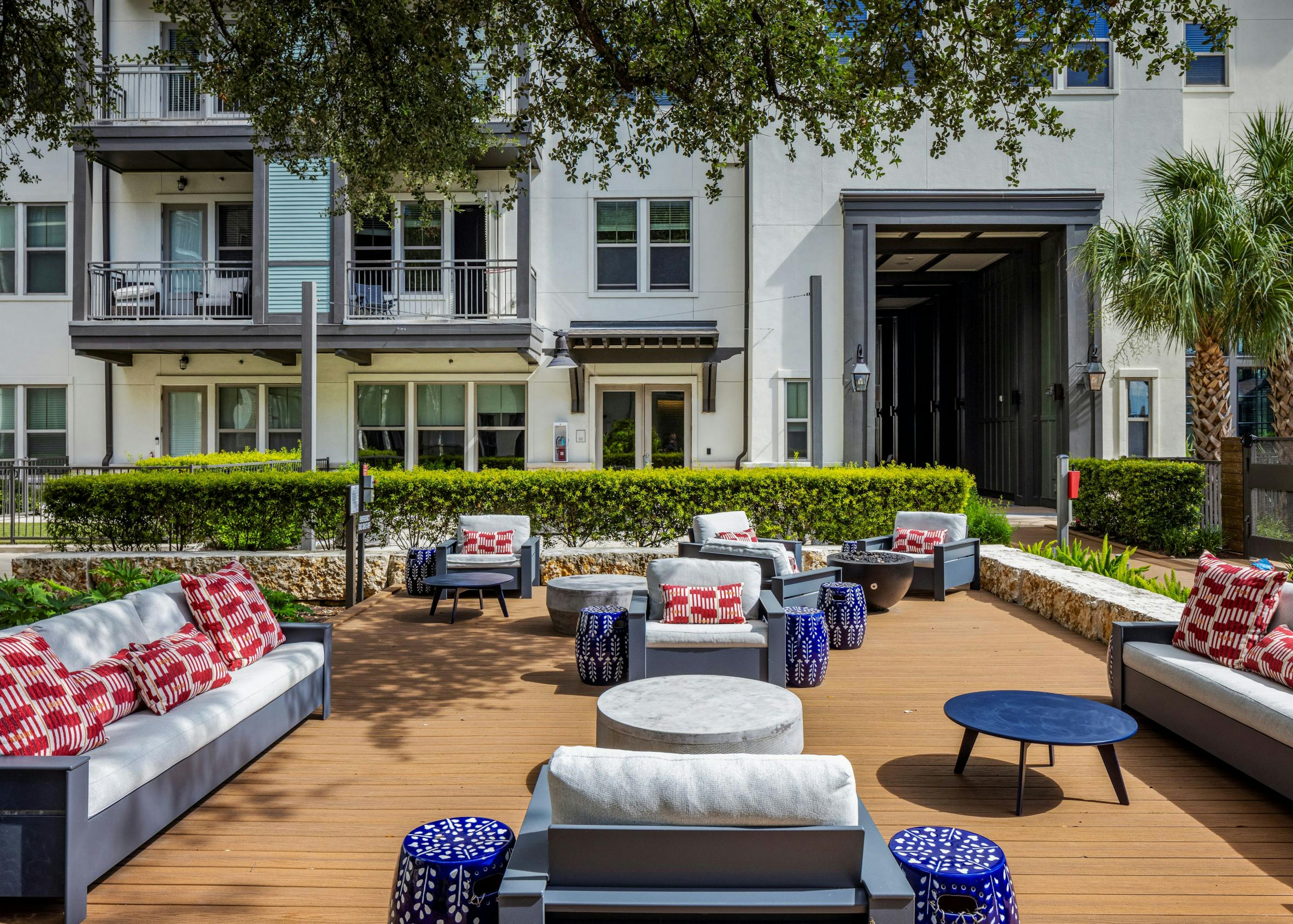 A large sunny outdoor lounge at AMLI Lakeline apartments with cushioned seating and red and white pillows and blue and white side tables