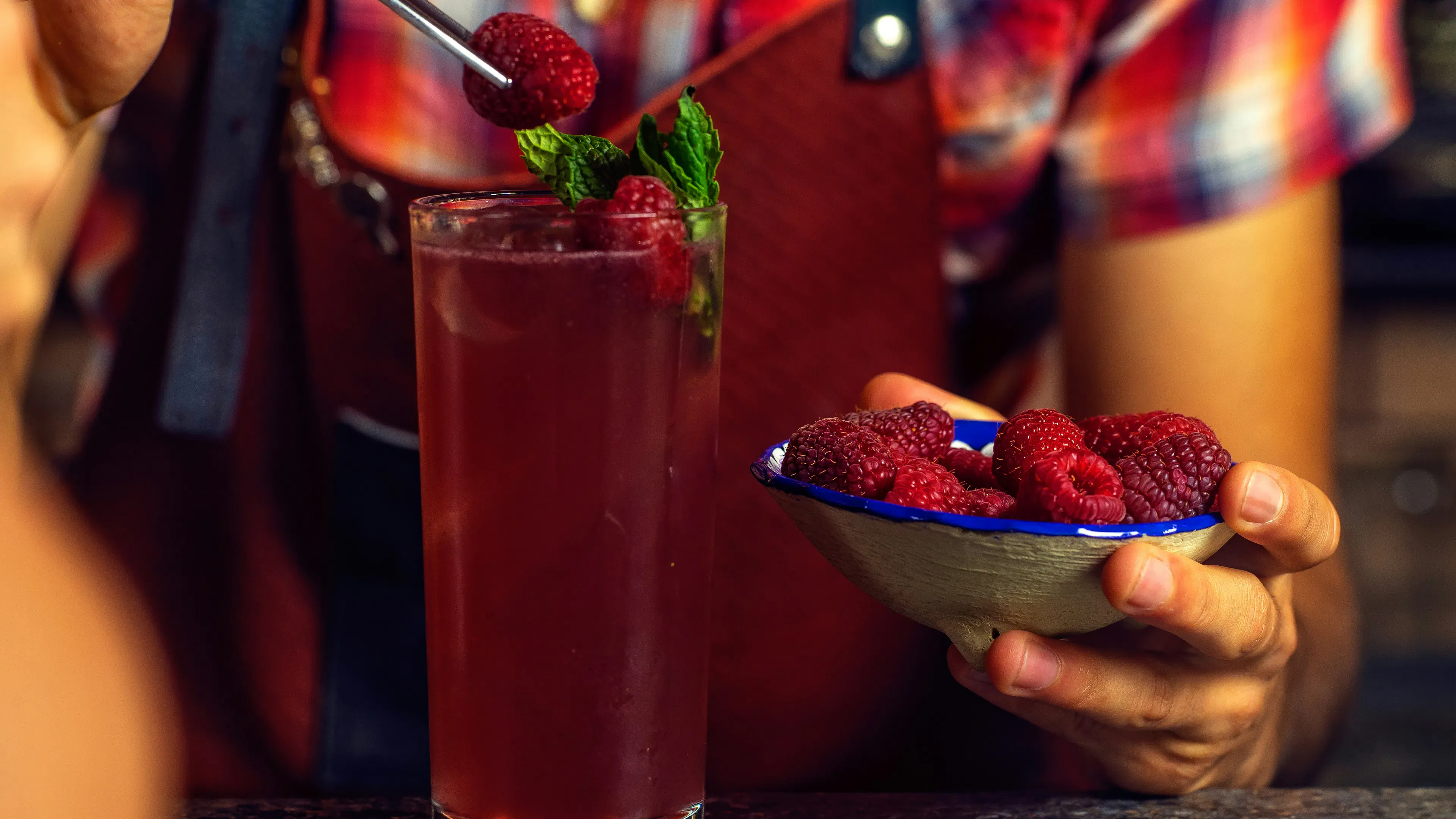 A tall glass filles with a berry flavored cocktail topped with fresh berries
