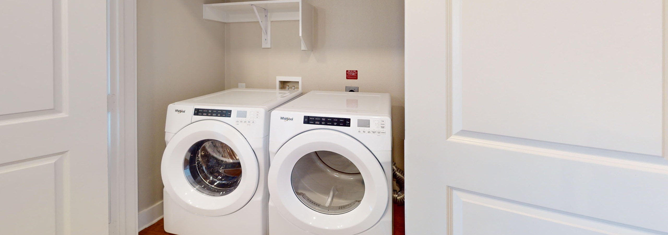 Open closet featuring a side by side front loading washer and dryer with shelves above at AMLI North Park apartments