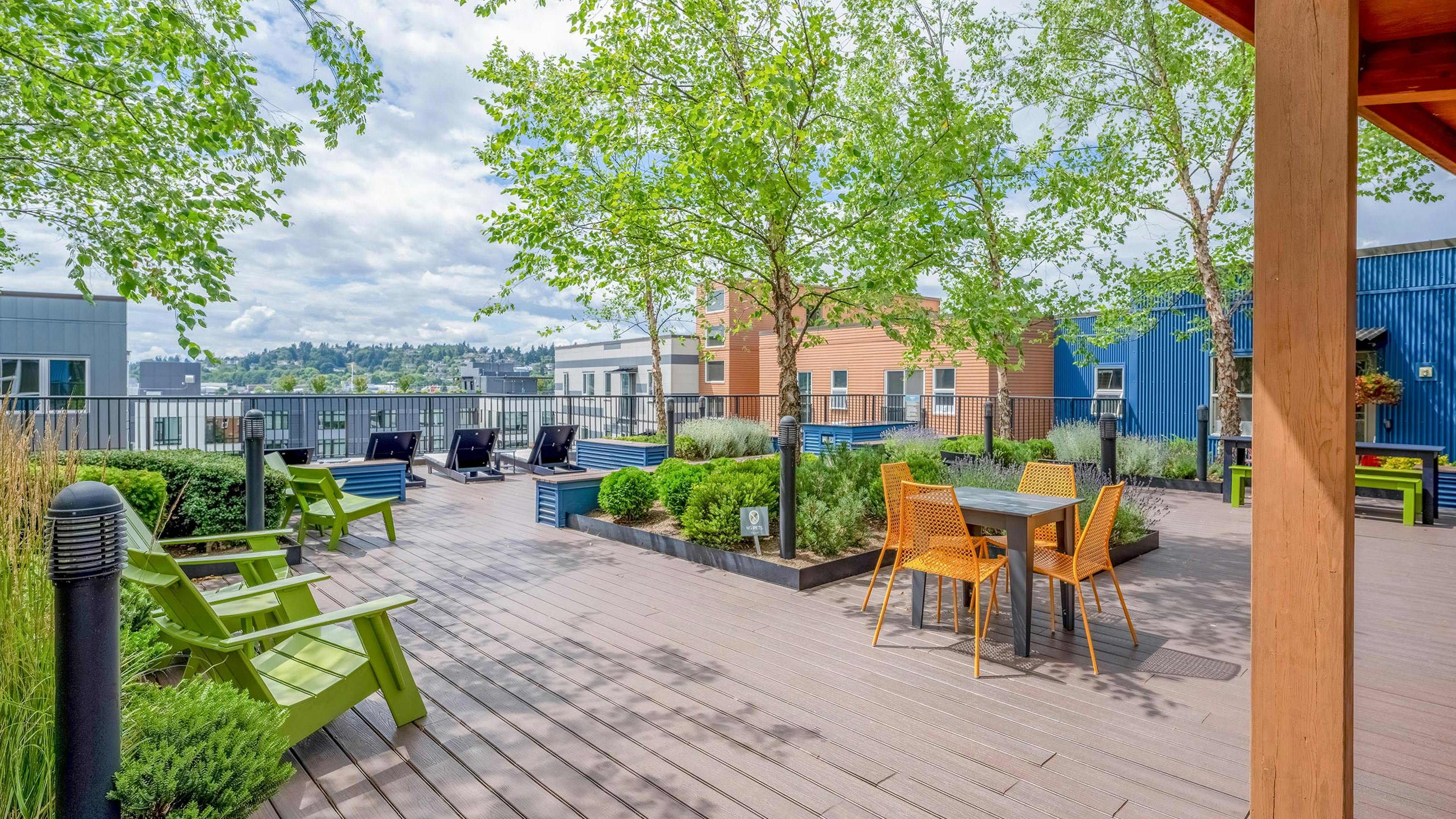 AMLI Mark24 apartments rooftop featuring wood deck flooring with green Adirondack chairs, a table with orange chairs and greenery.