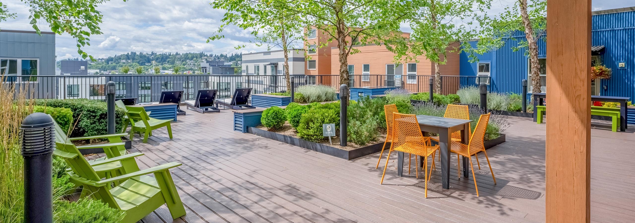 AMLI Mark24 apartments rooftop featuring wood deck flooring with green Adirondack chairs, a table with orange chairs and greenery.