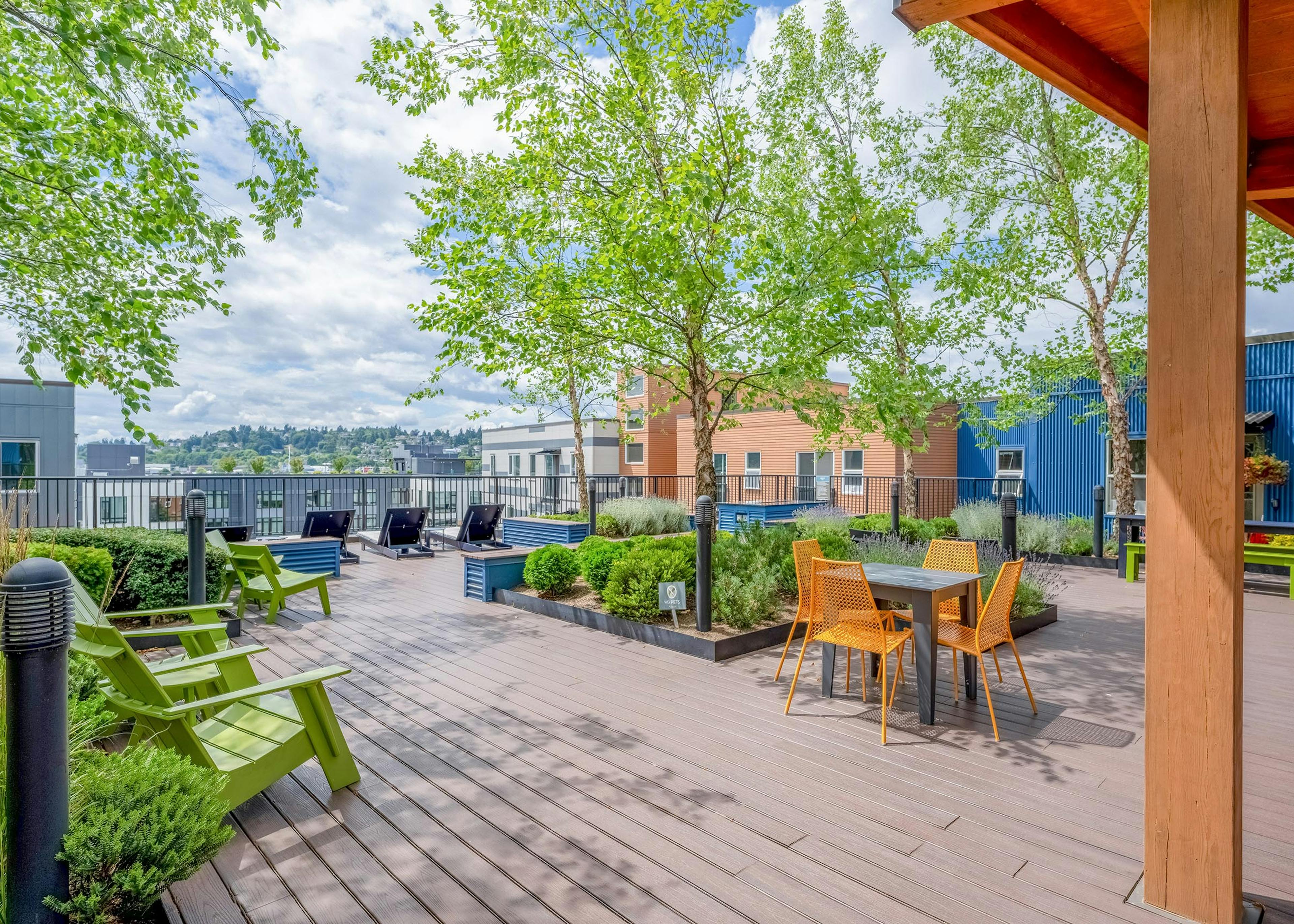 AMLI Mark24 apartments rooftop featuring wood deck flooring with green Adirondack chairs, a table with orange chairs and greenery.