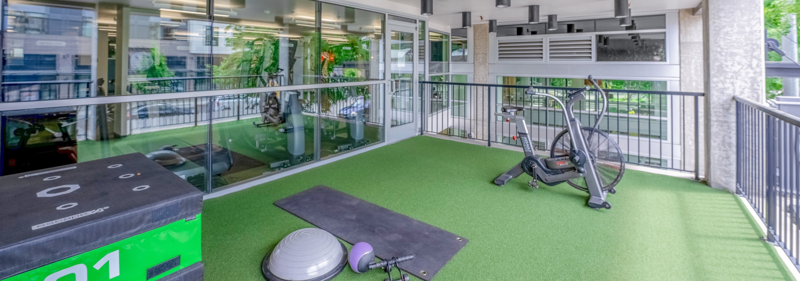 AMLI Mark24 outdoor fitness area with artificial grass flooring and featuring various exercise equipment and stationary bike.