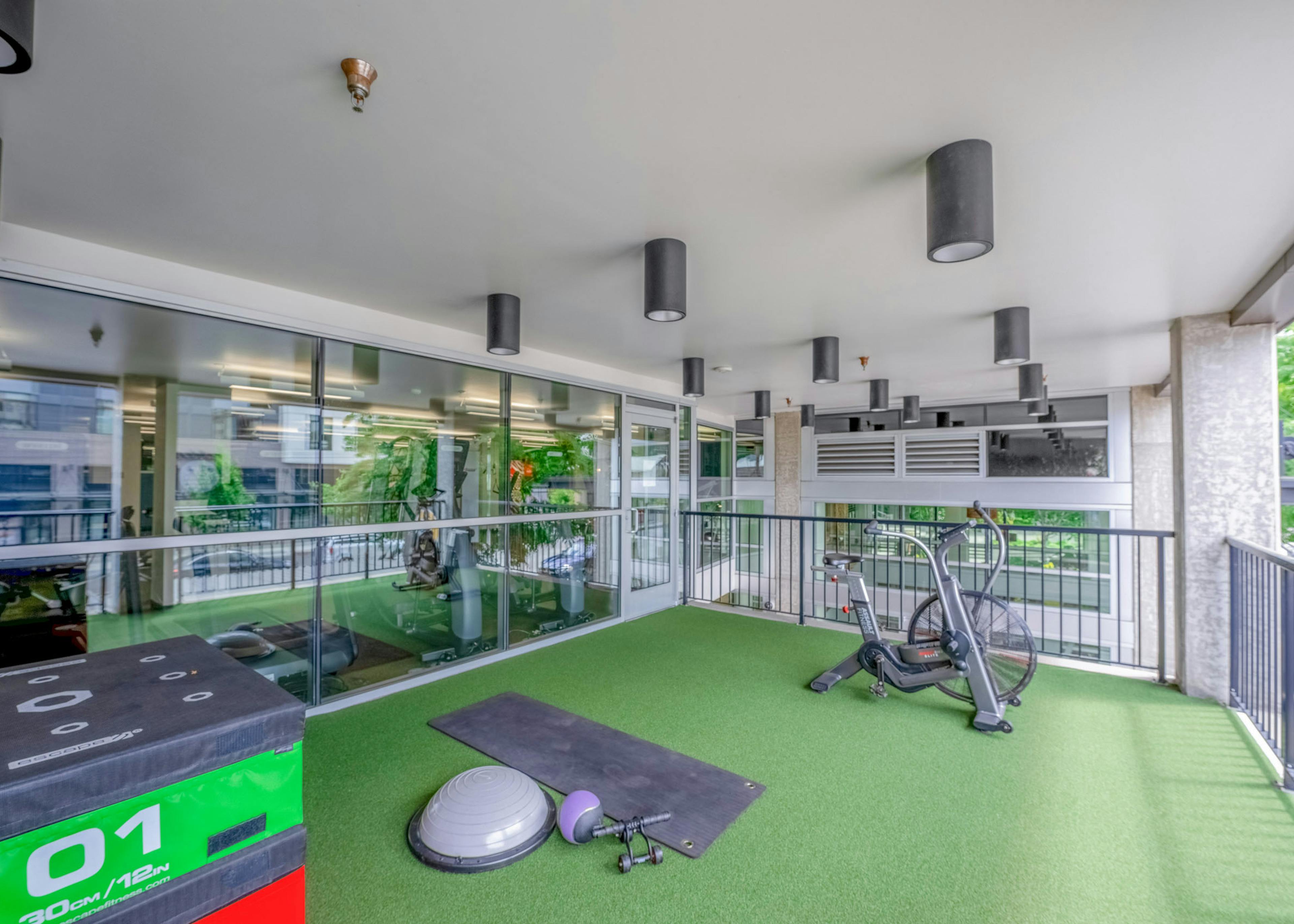 AMLI Mark24 outdoor fitness area with artificial grass flooring and featuring various exercise equipment and stationary bike.