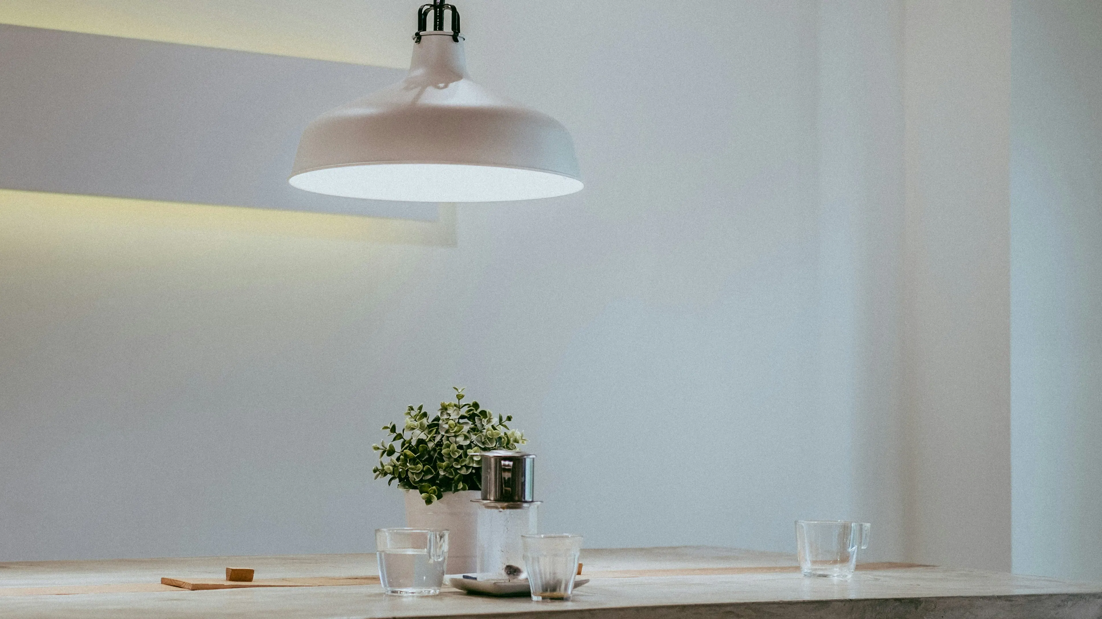 An elegant white light hanging over a simple wooden table with a small plant in the center