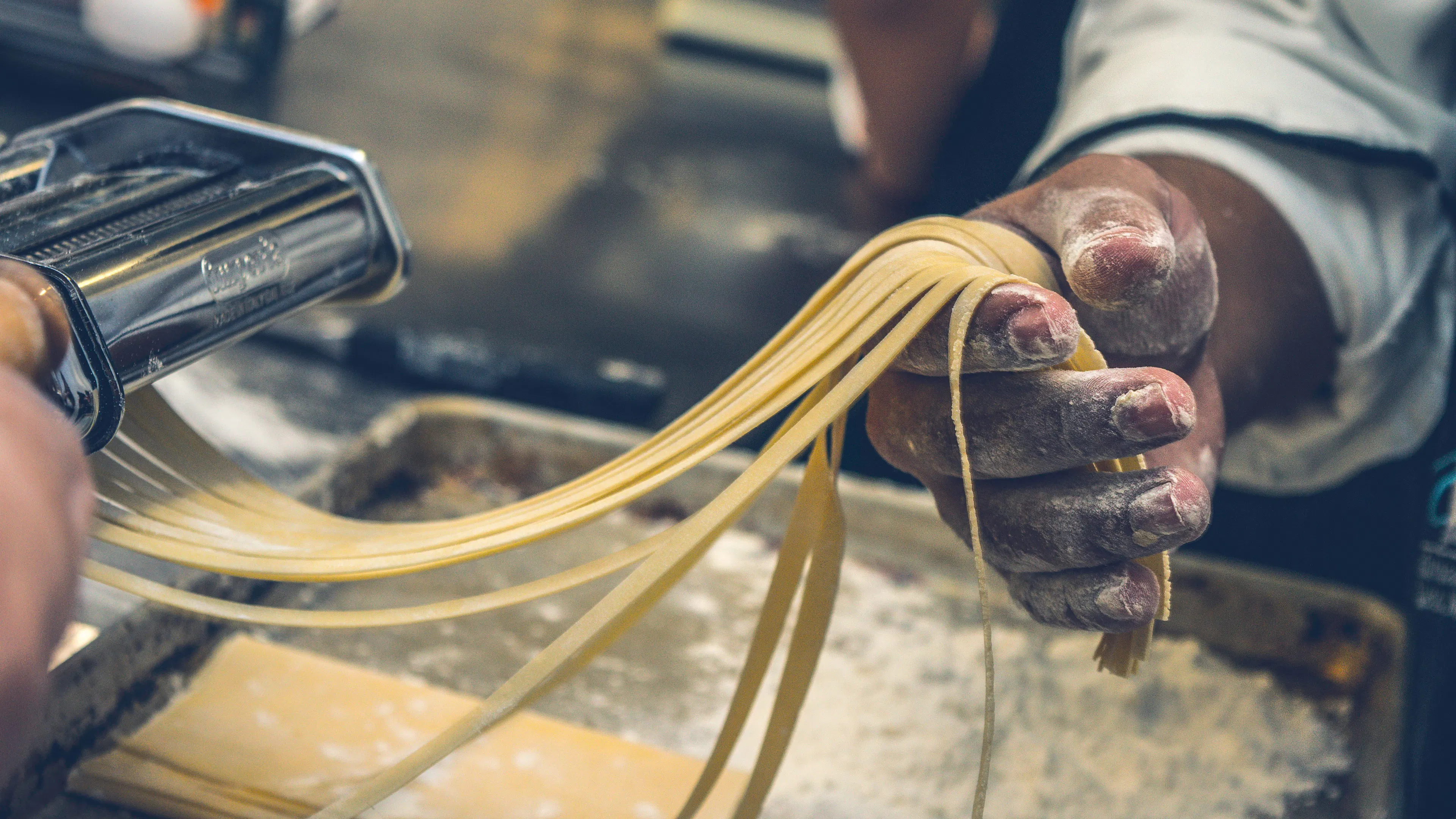 A chef's hand holding some pasta straight out of a pasta machine