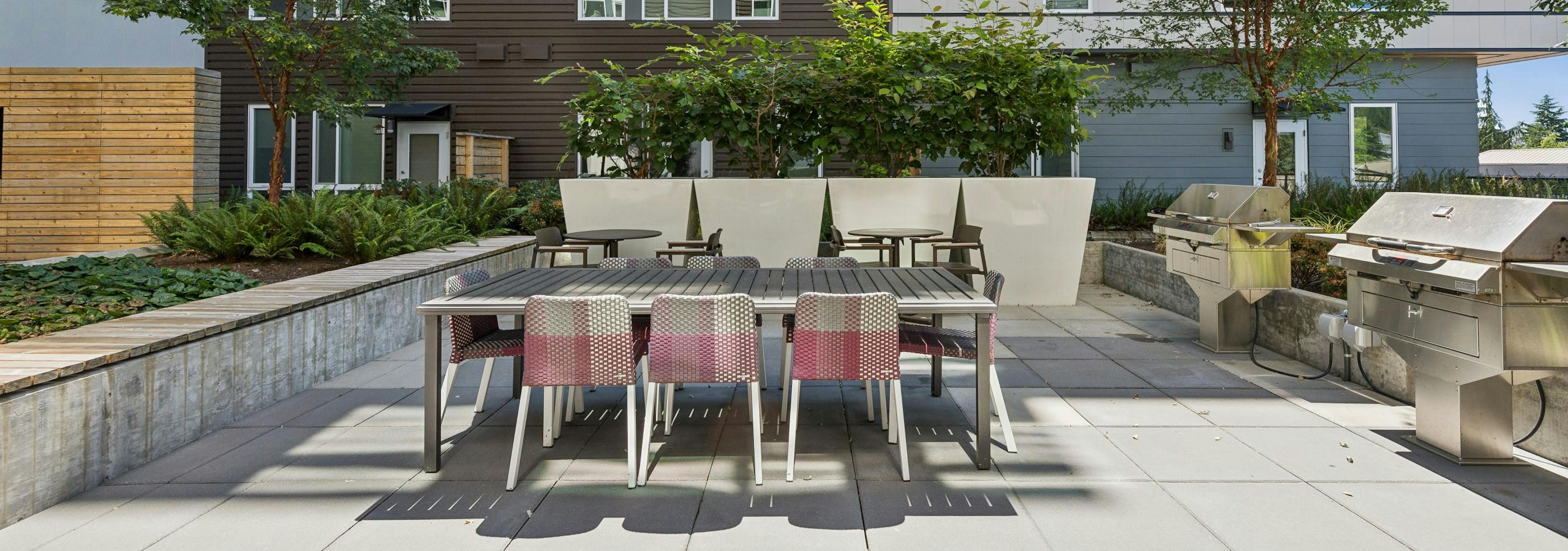Courtyard with large table with 8 chairs adjacent to 2 stainless steel grills at AMLI Spring District apartments