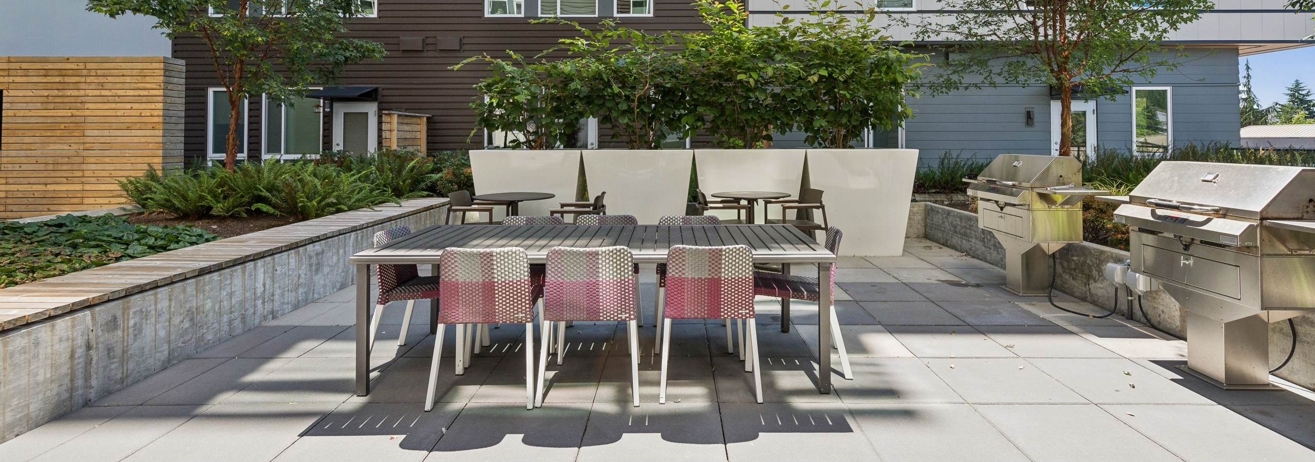 Courtyard with large table with 8 chairs adjacent to 2 stainless steel grills at AMLI Spring District apartments