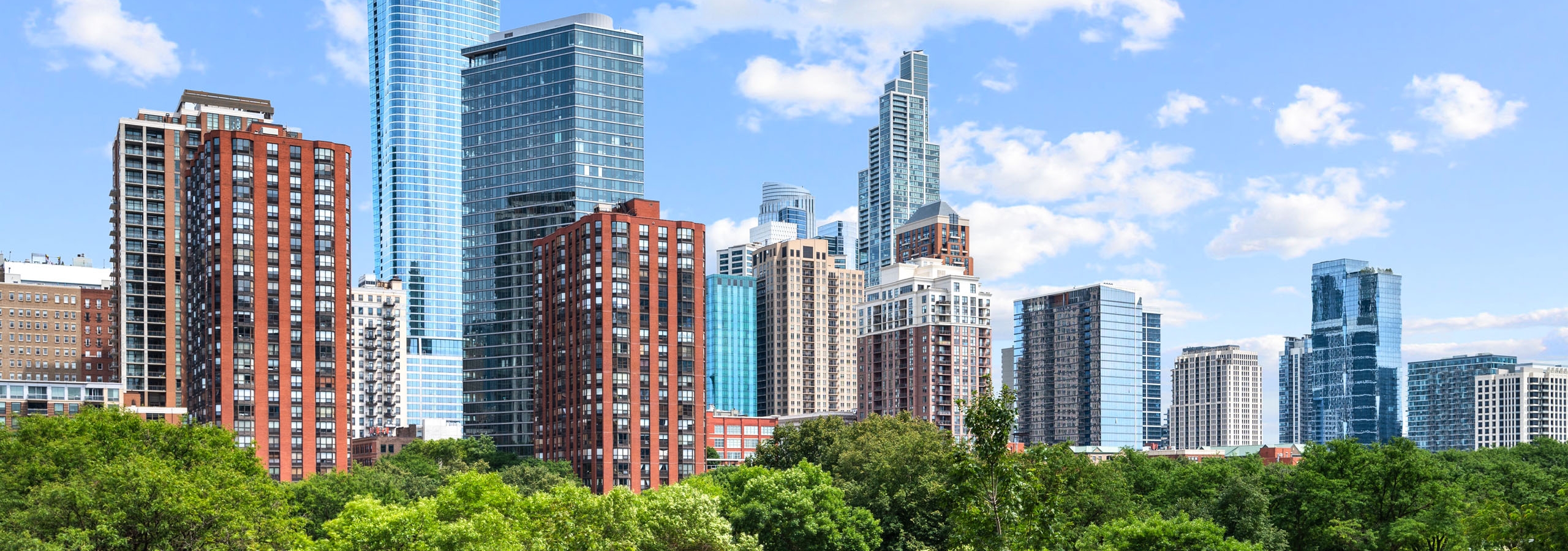 AMLI Lofts view of tree lined street in front of Chicago skyline with fluffy white clouds dotting the blue sky.